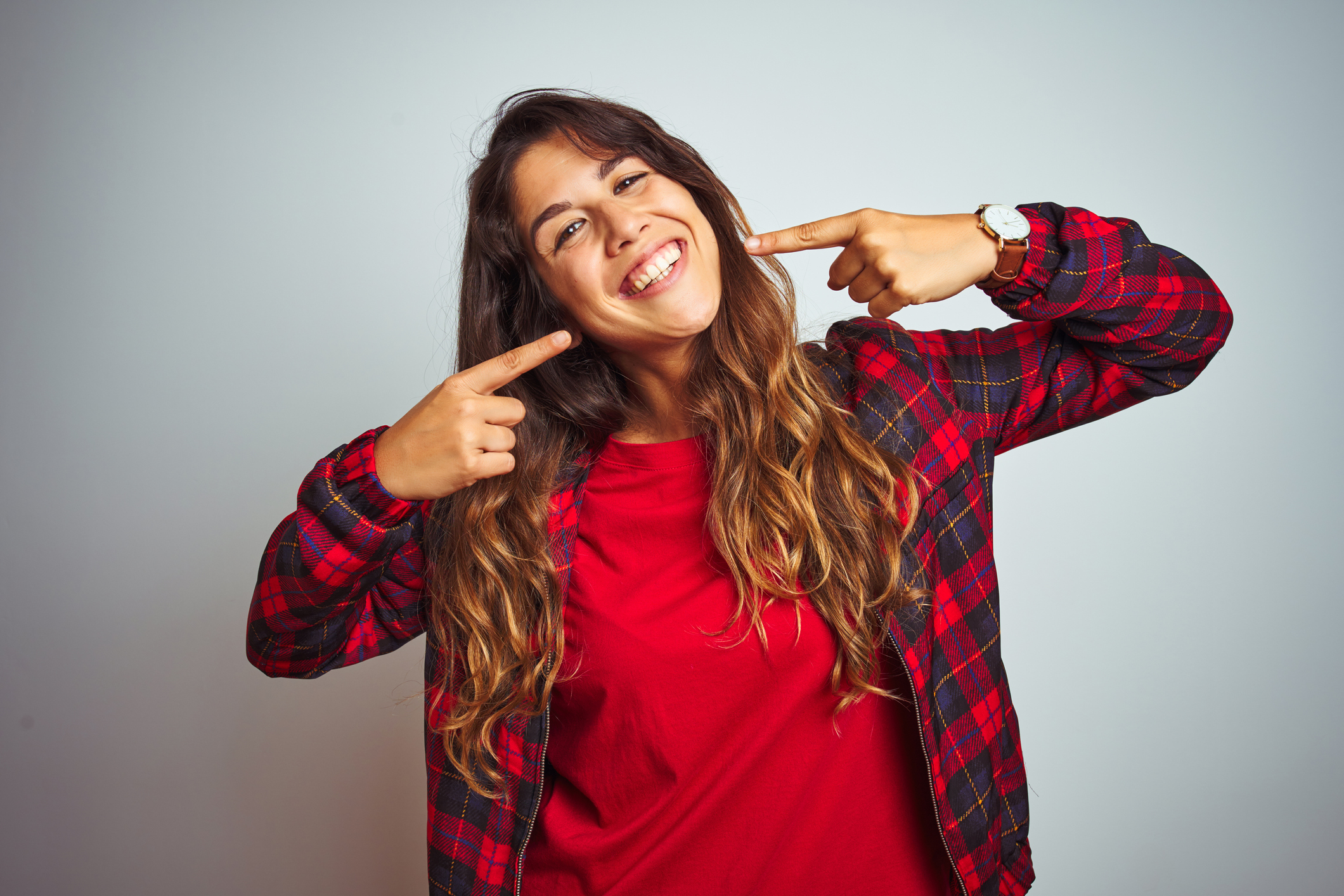 Young beautiful woman wearing red t-shirt and jacket standing over white isolated background smiling cheerful showing and pointing with fingers teeth and mouth. Dental health concept.