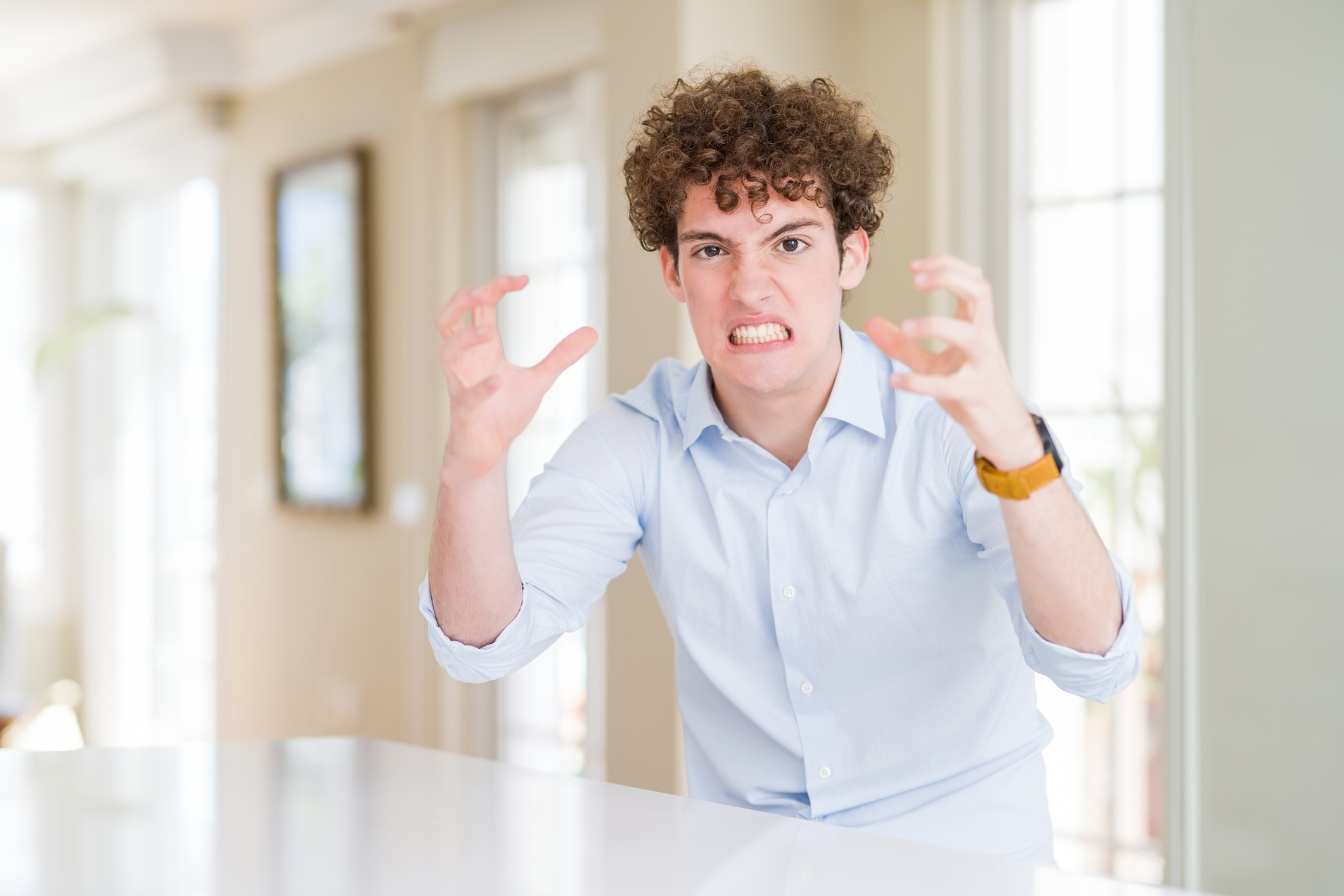 Young business man with curly read head Shouting frustrated with rage, hands trying to strangle, yelling mad