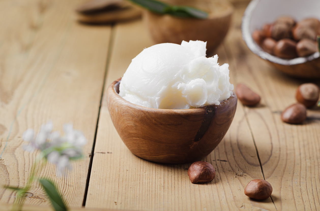 Shea butter in wooden bowl with nuts on old rustic table. Free text space.