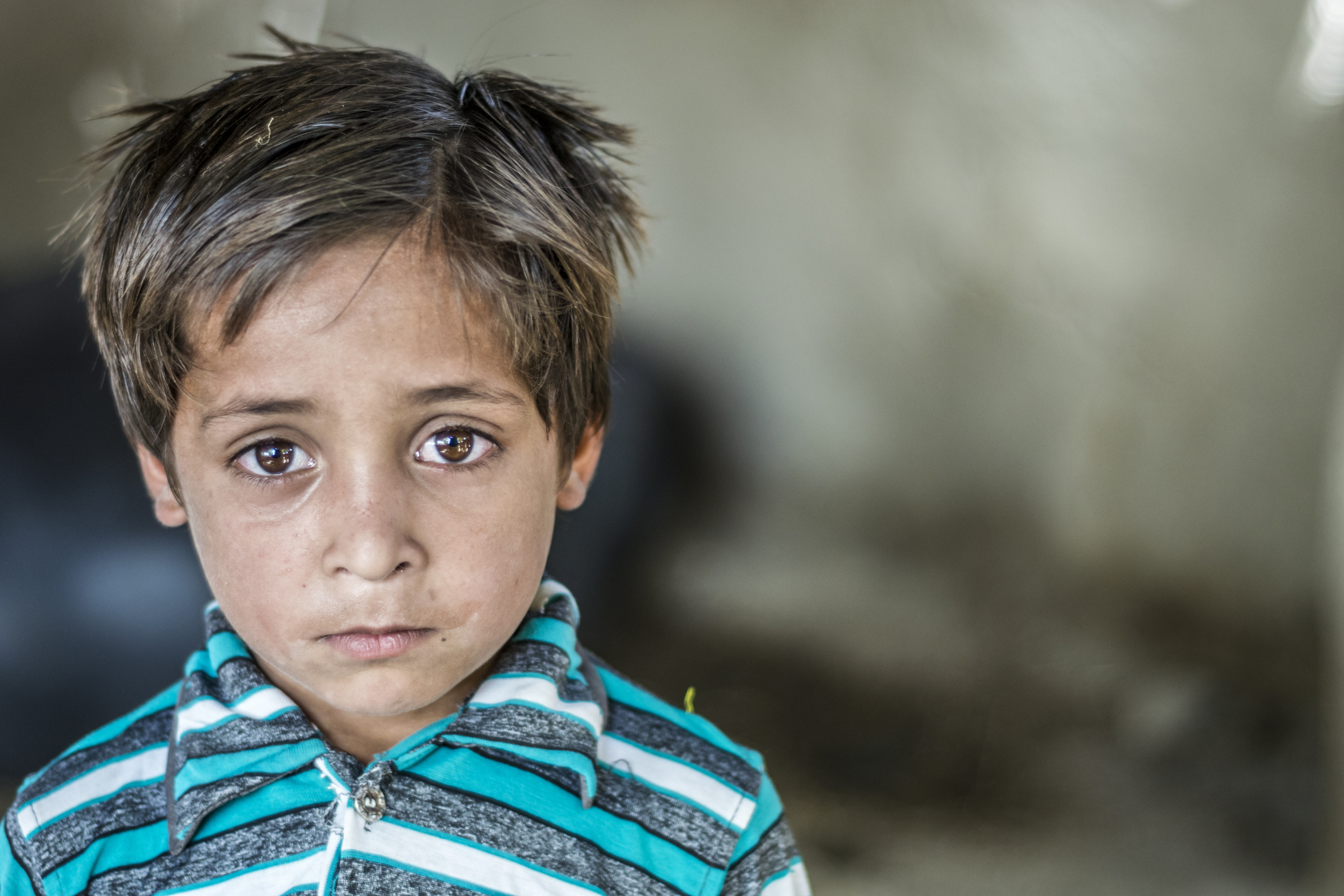 closeup of a poor staring hungry orphan boy in a refugee camp with sad expression on his face and his face and clothes are dirty and his eyes are full of pain