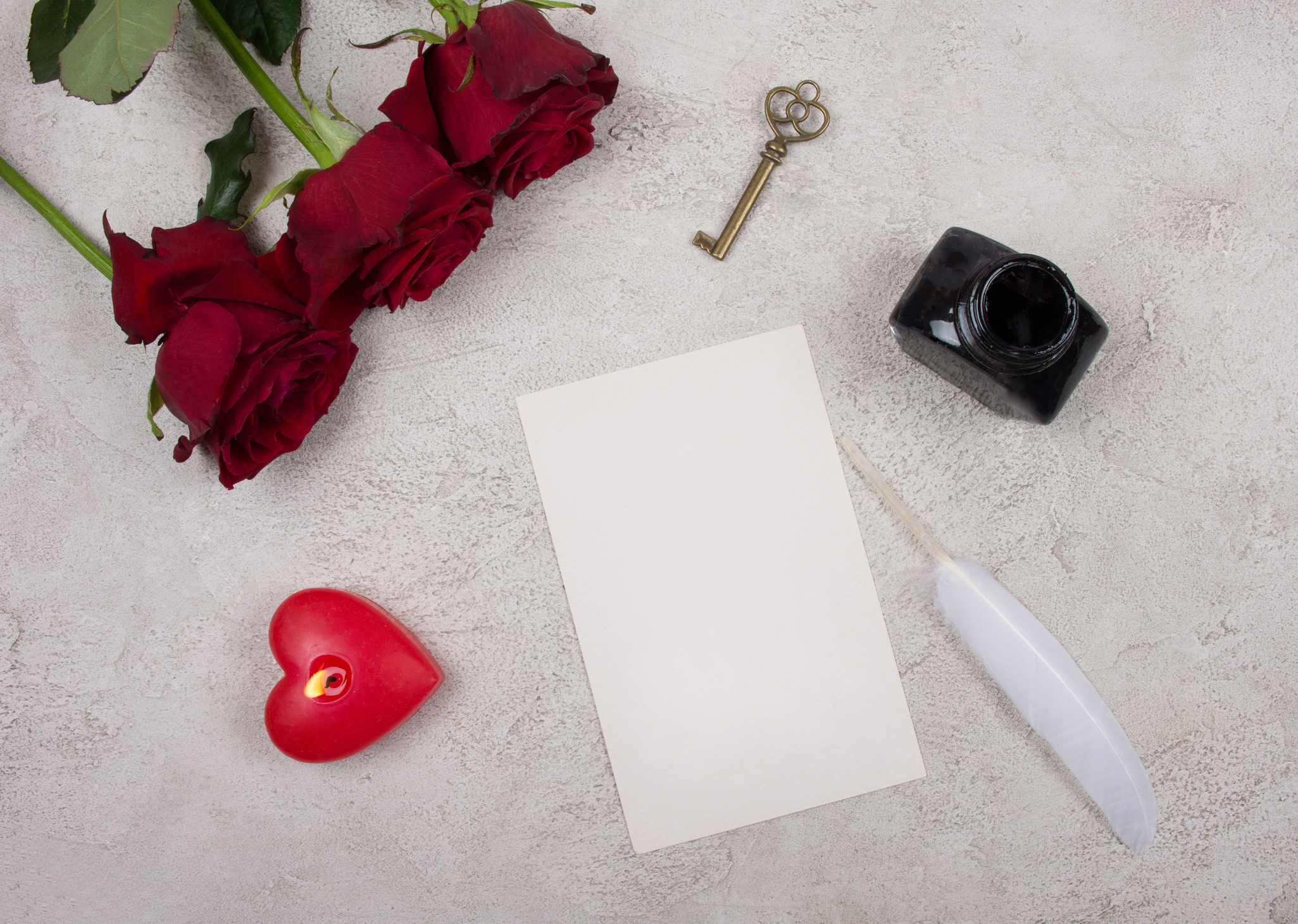 Red roses, a heart-shaped candle, a key, a blank card, a white feather and an inkpot