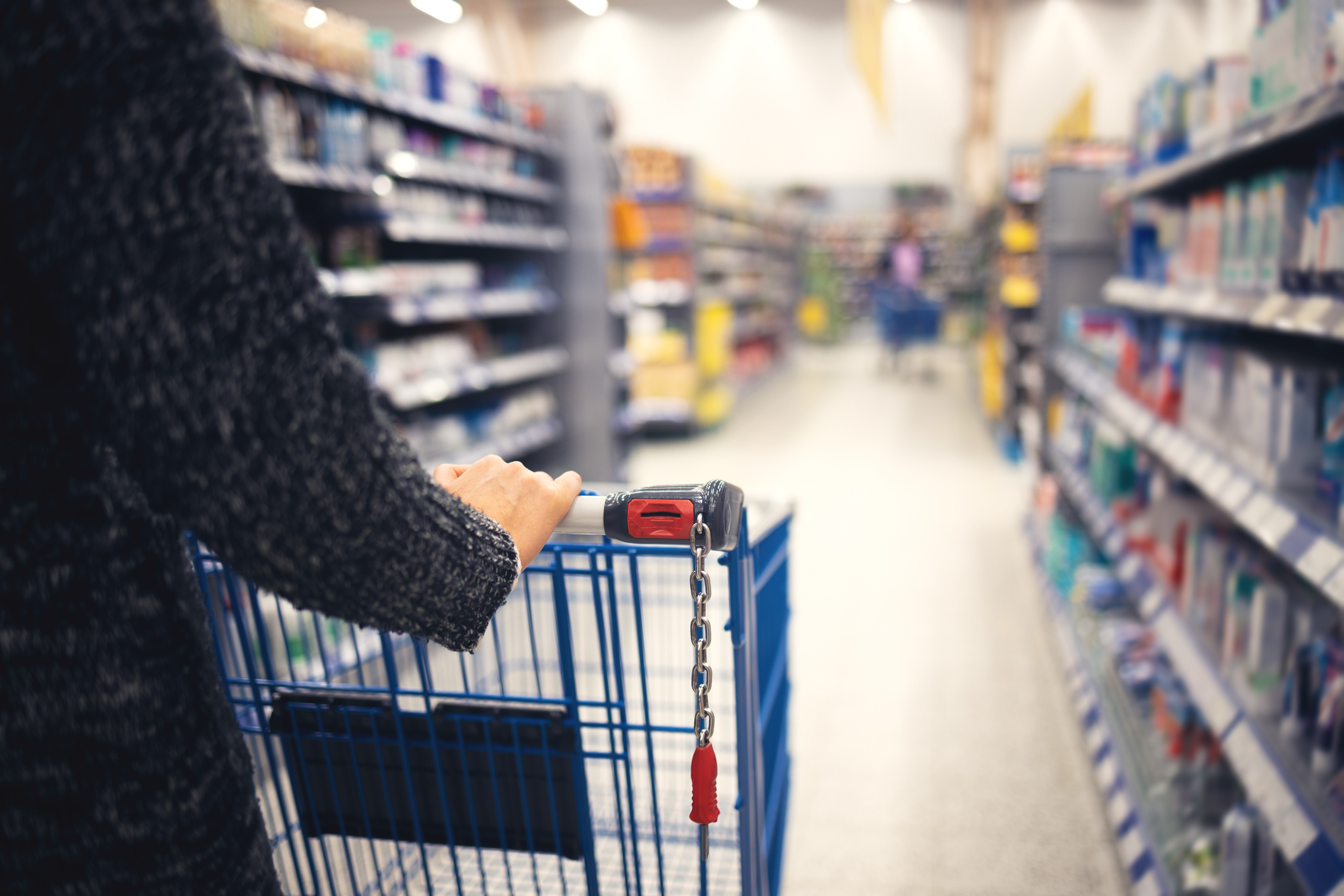 A women walks with a shopping basket in a store. Hand and part of the basket in focus