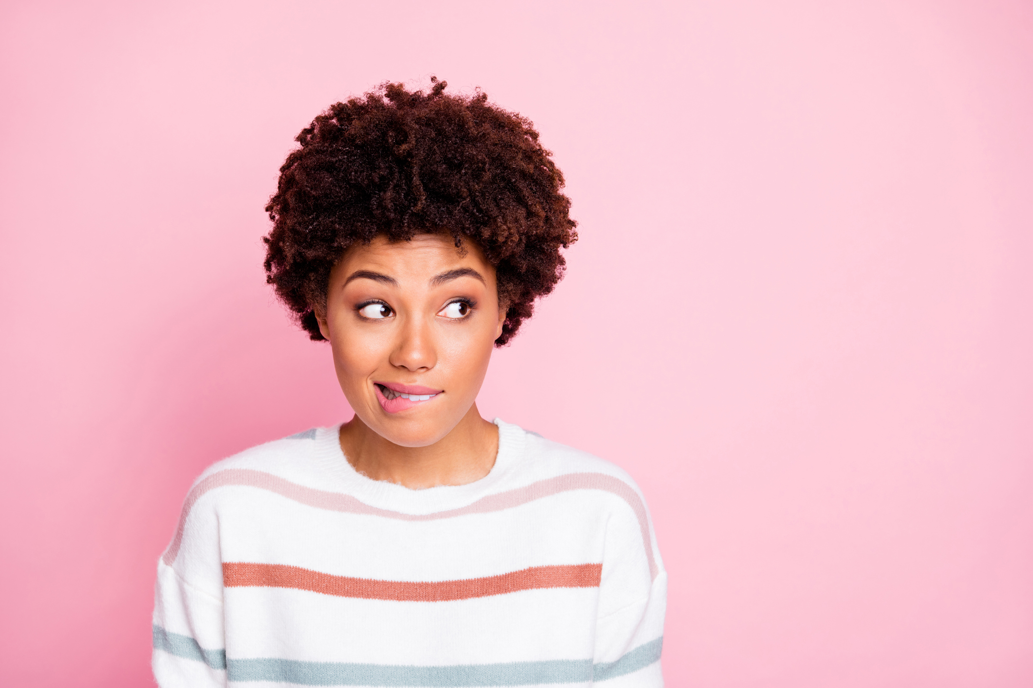 Photo of anxious thinking guessing black girl biting her lips staring away at empty space with misunderstanding face expression isolated over pink pastel color background