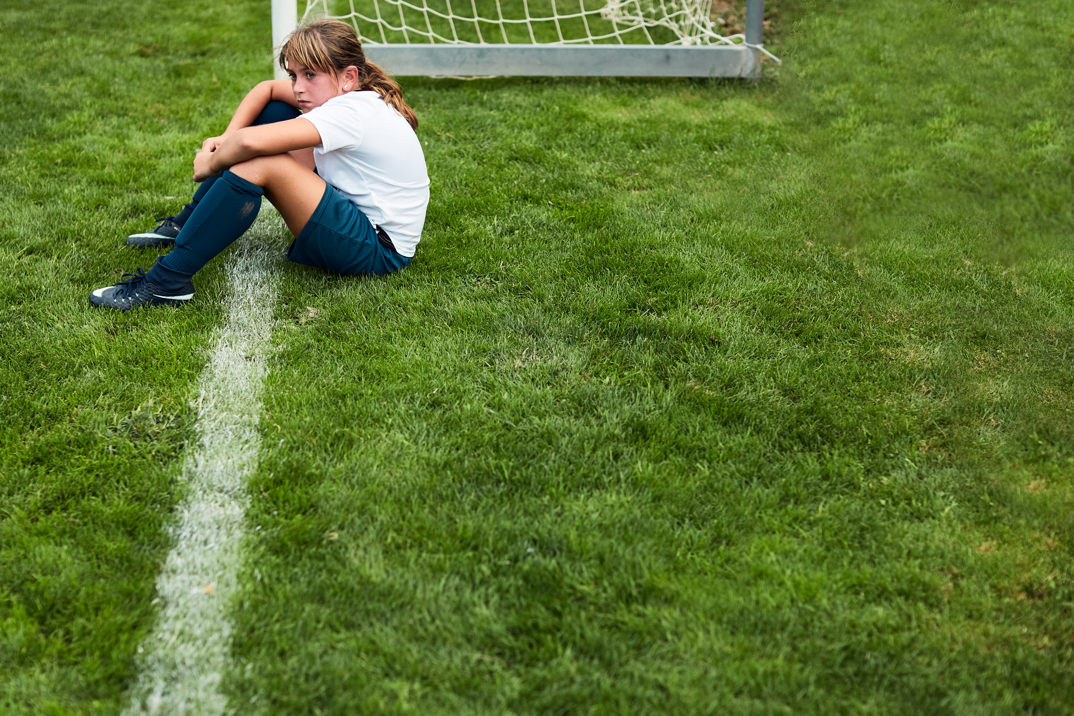 Young girl sitting on the grass after a match defeat.