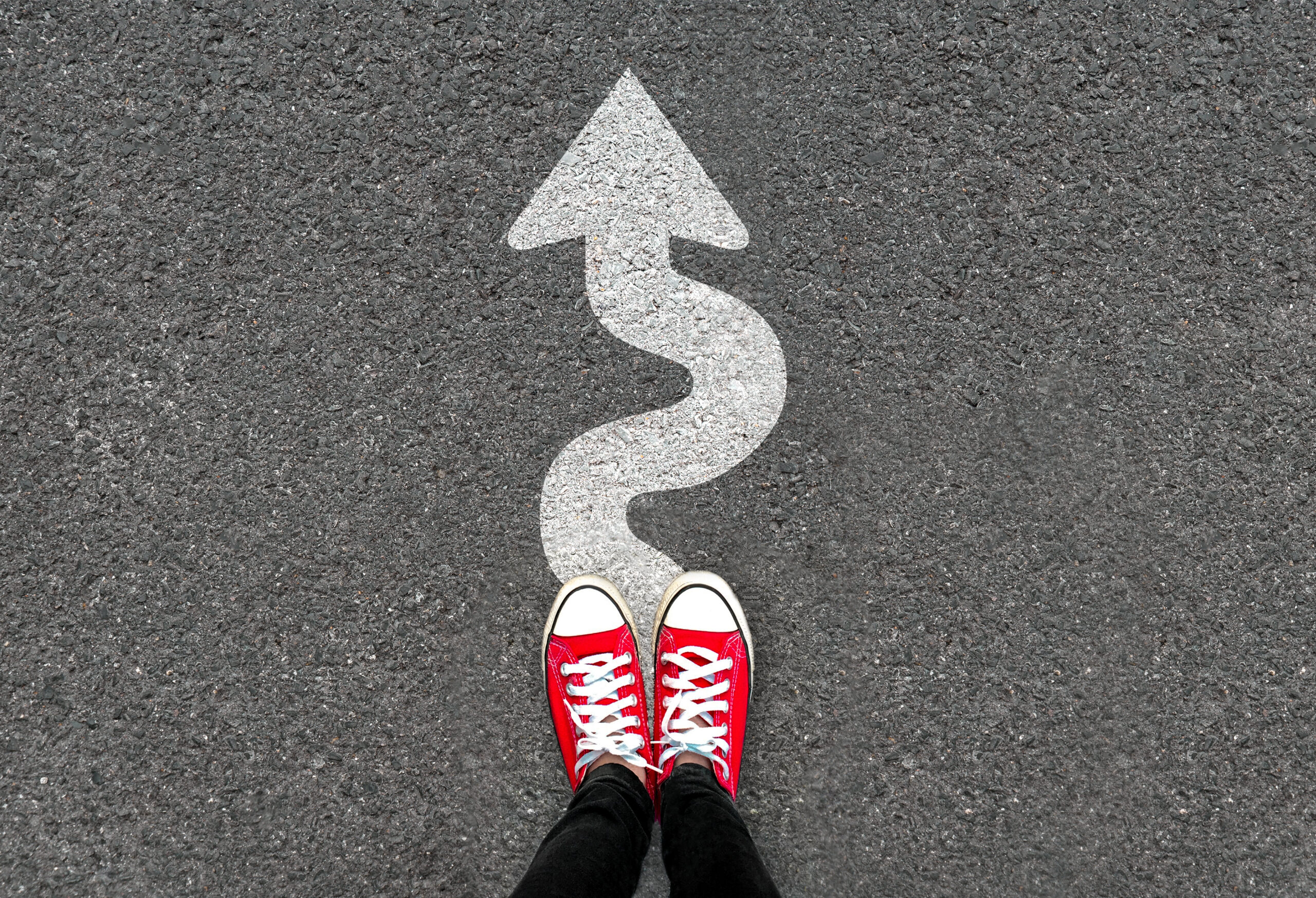 Feet and white arrow sign go straight on road background. Top view of woman. Forward movement and motivation idea concept.