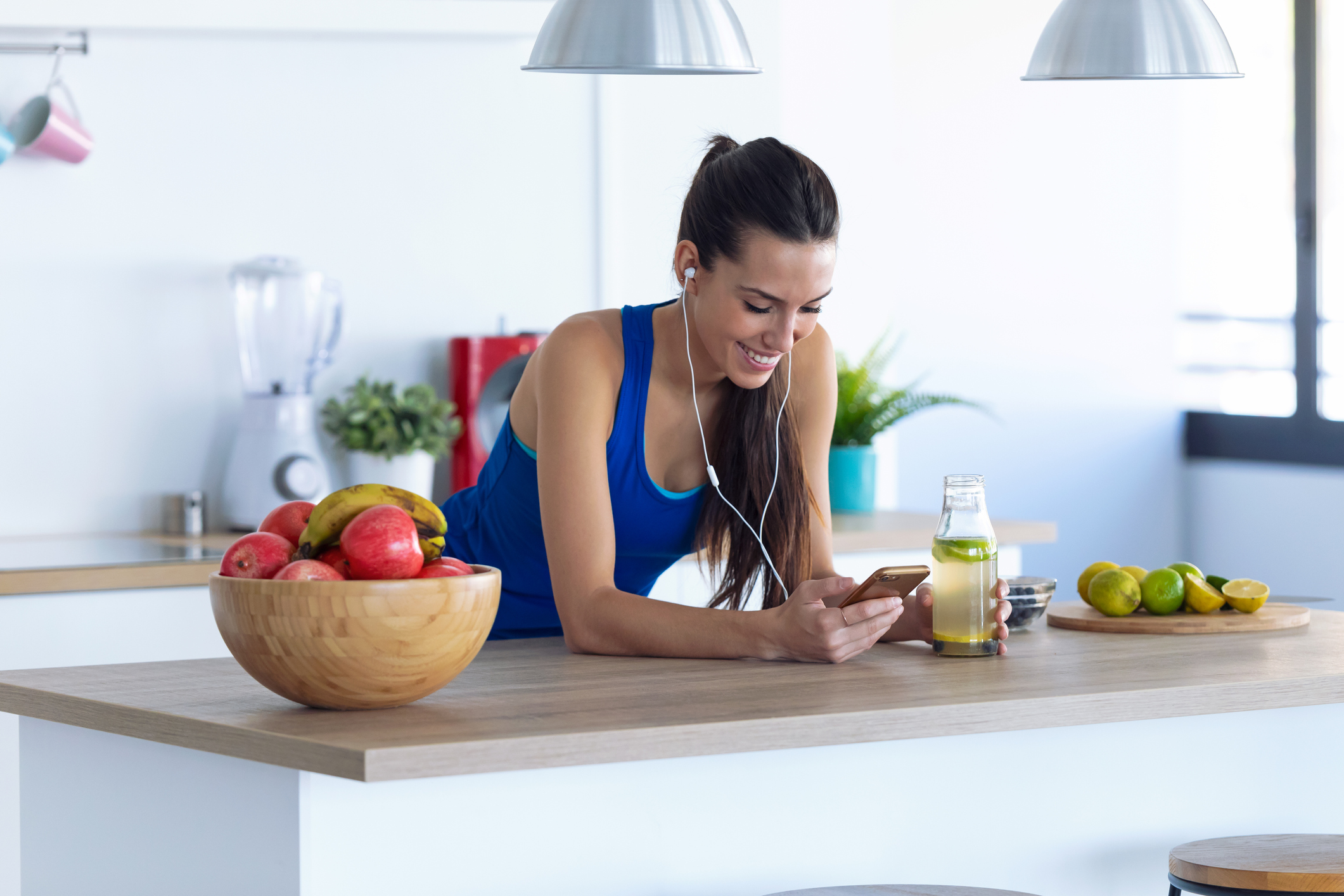 Sporty young woman listening to music with mobile phone after training in the kitchen at home.