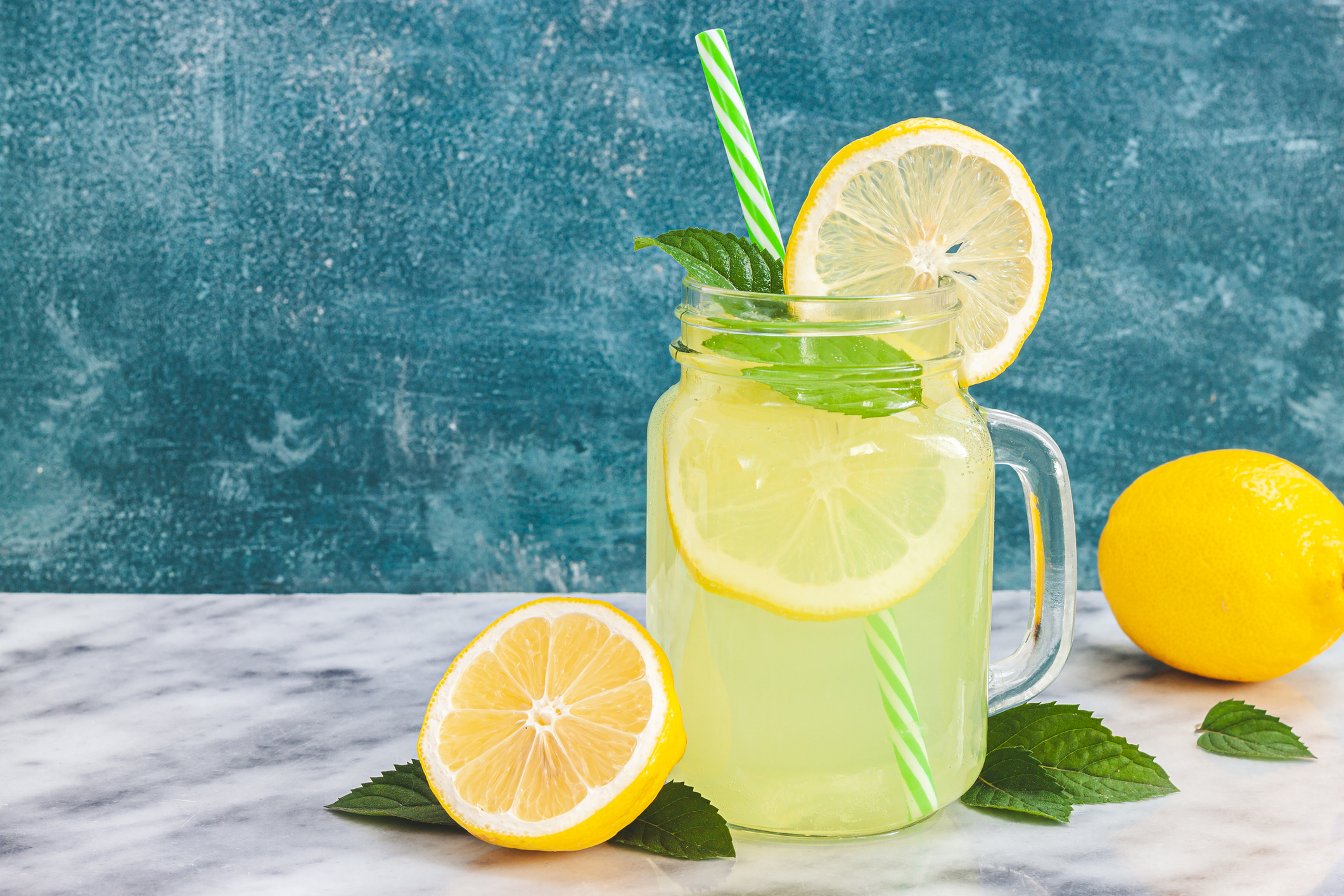 Lemon lemonade in mason jar glass ofwith lemons and straw on table background