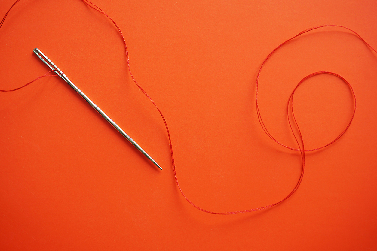 Needle with red thread on red background.