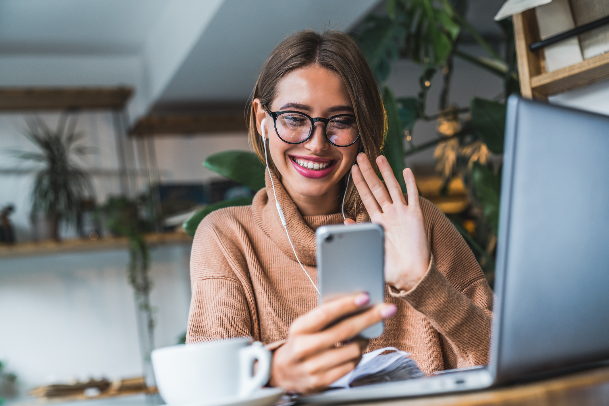 Young smilingwoman video chatting using earphones and mobile phone.