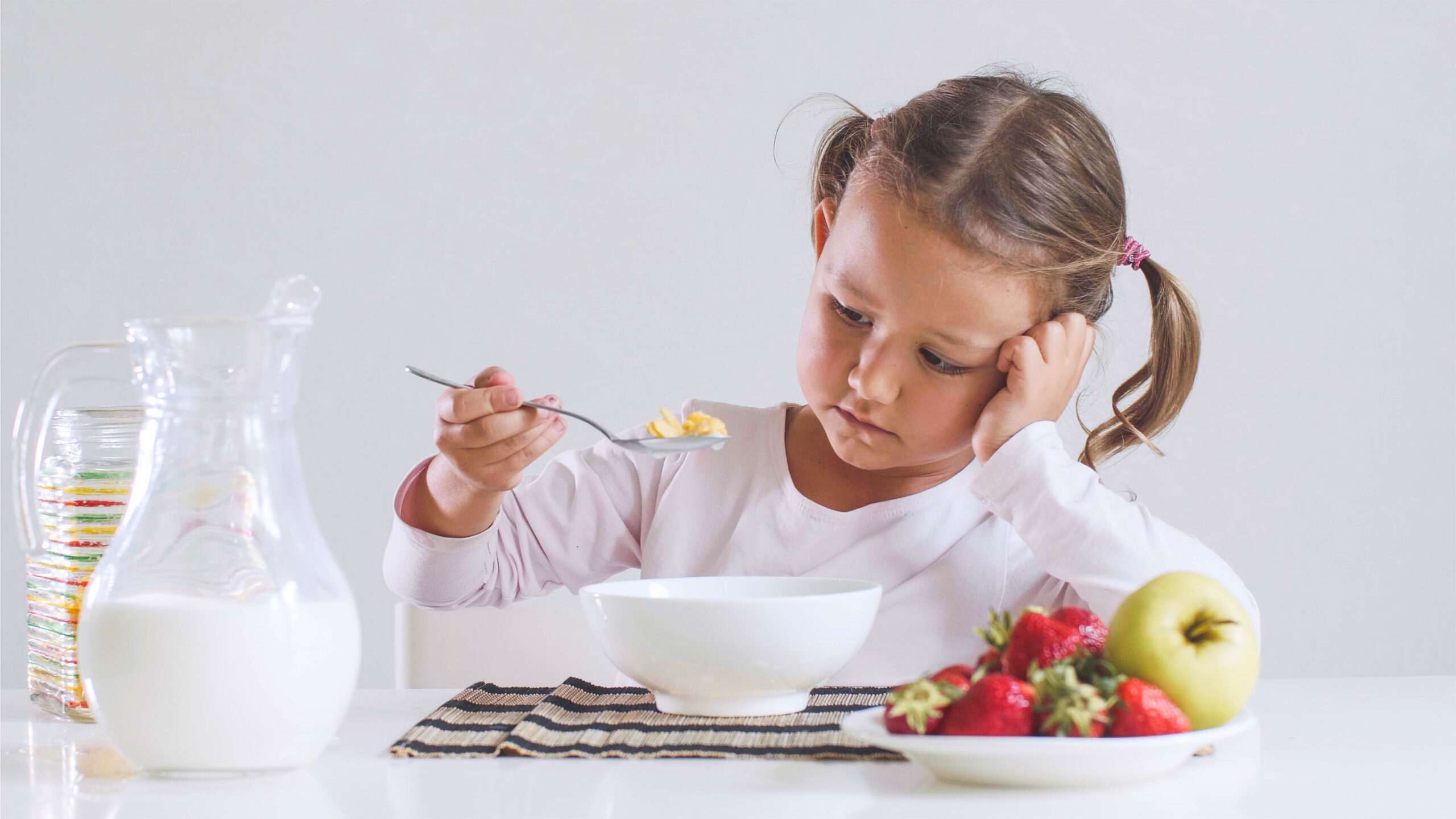 Bored little girl doesn't want to eat cornflakes with milk for breakfast.