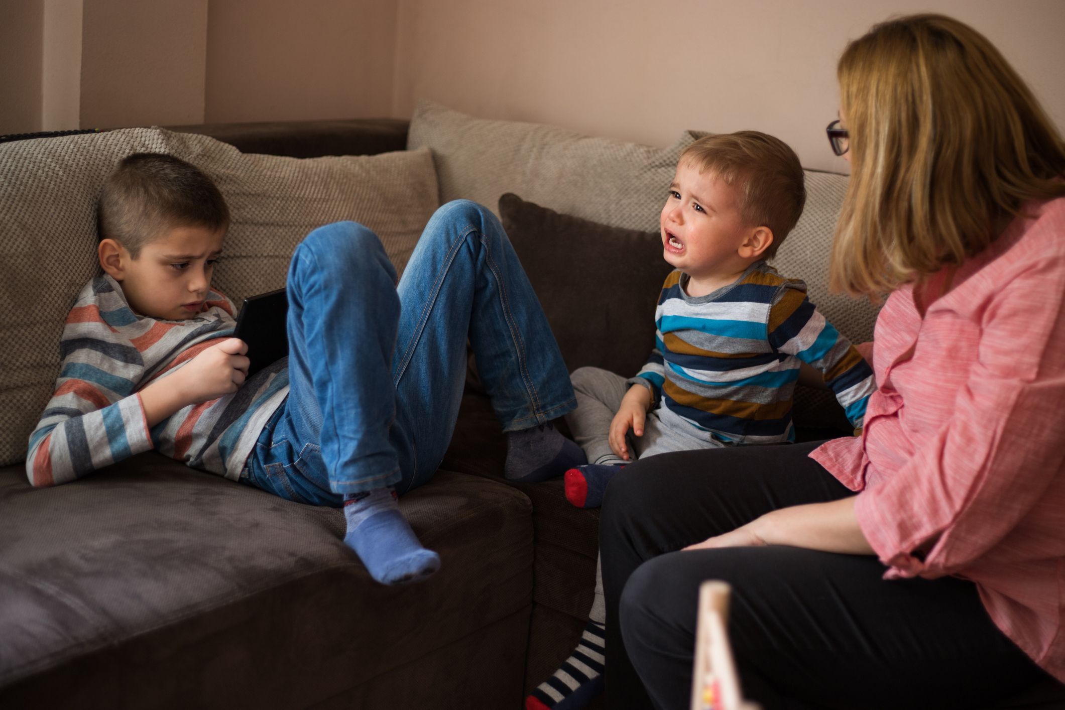 Crying toddler at home with his older brother and mother