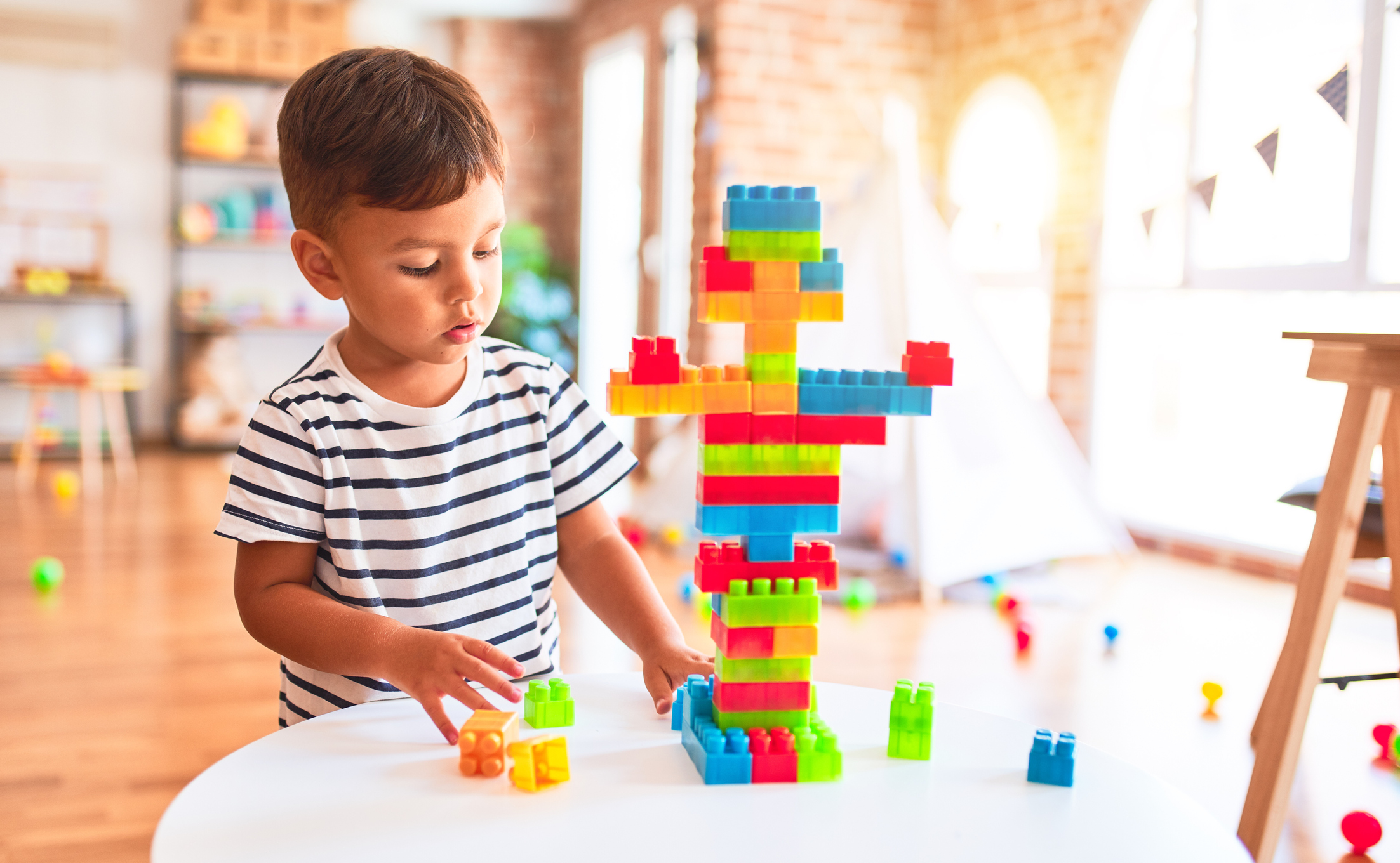 Beautiful toddler boy playing with construction blocks at kindergarten