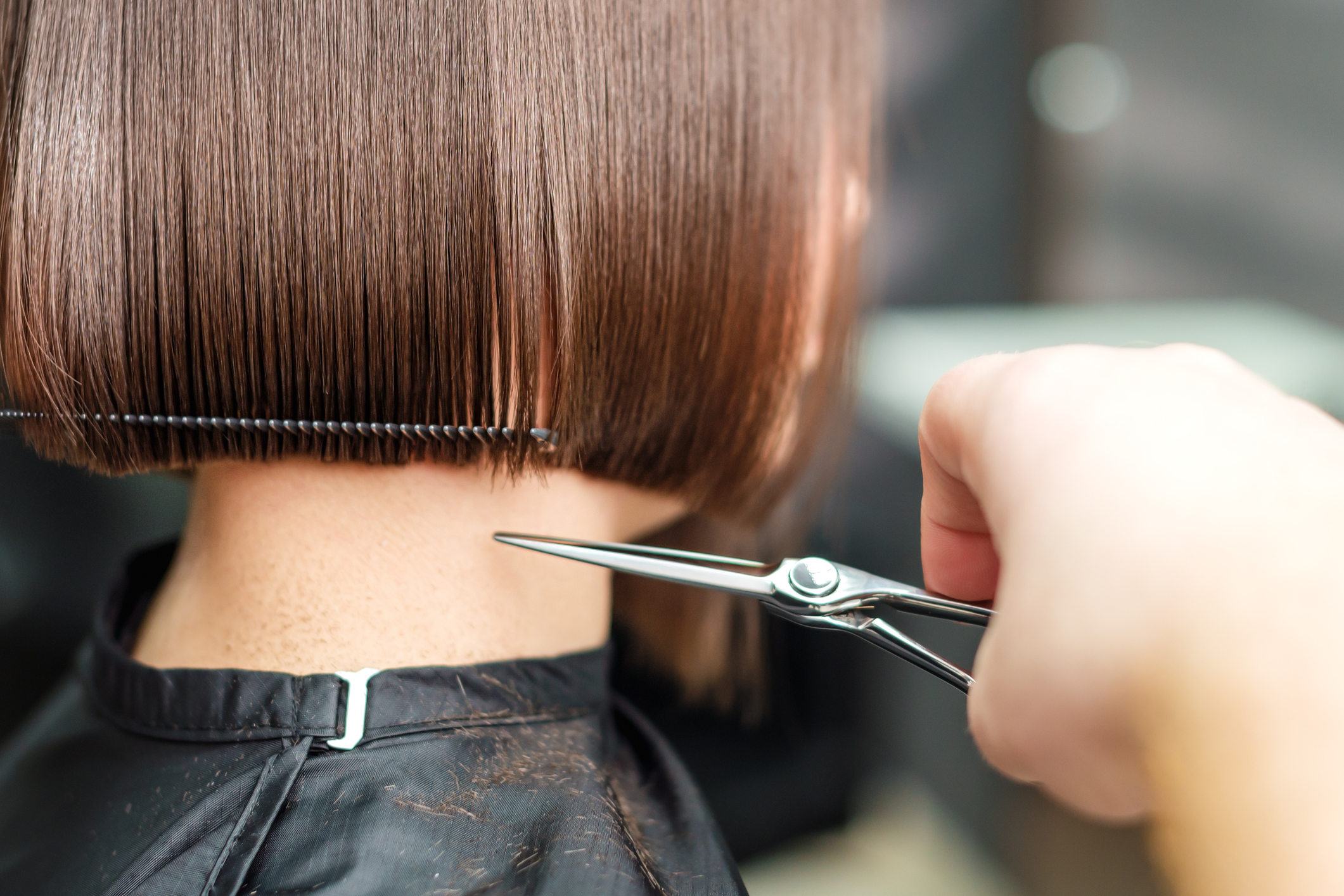 Hairdresser's hands are cutting brown short hair.