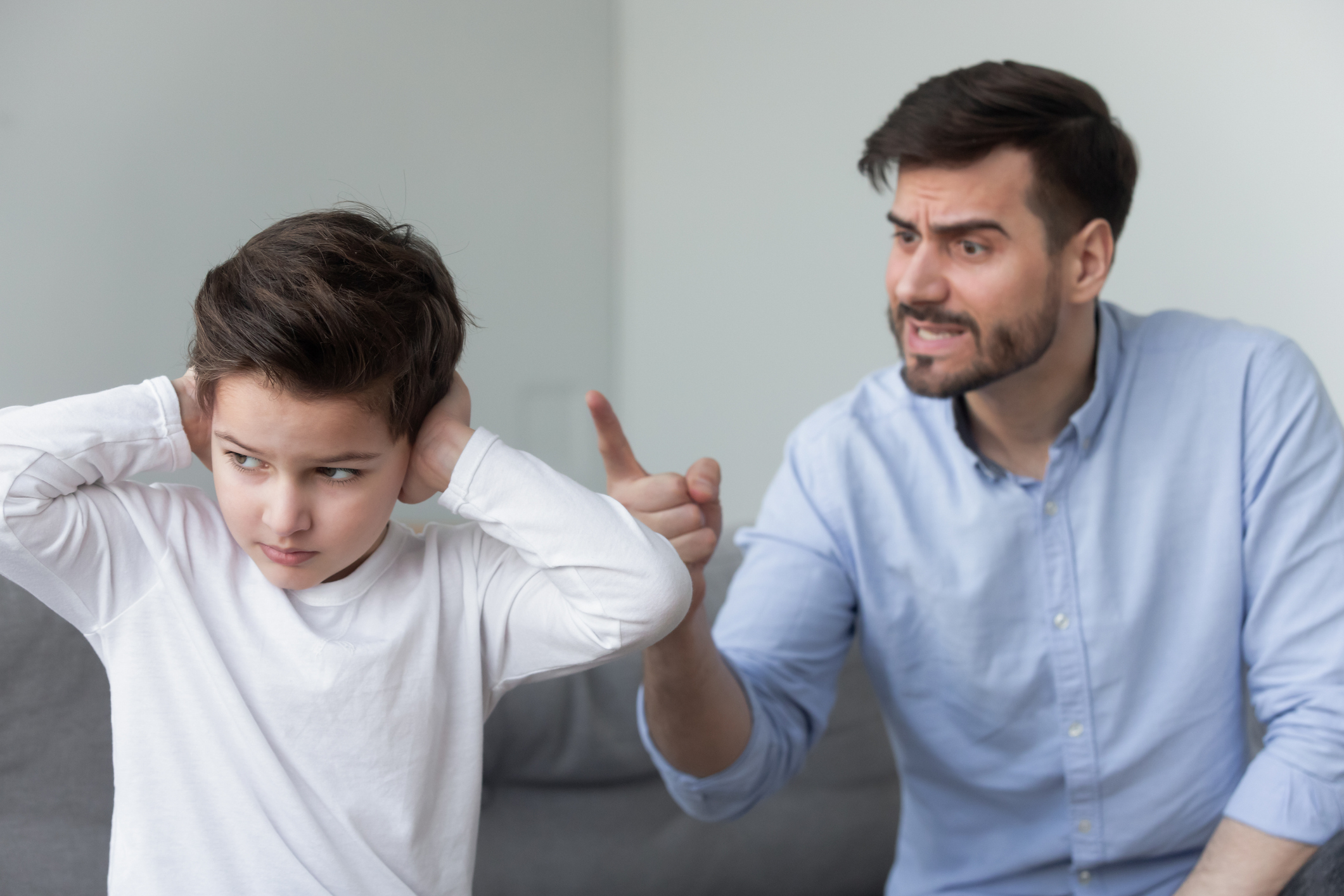 Angry father shouting at stubborn fussy little son closing ears