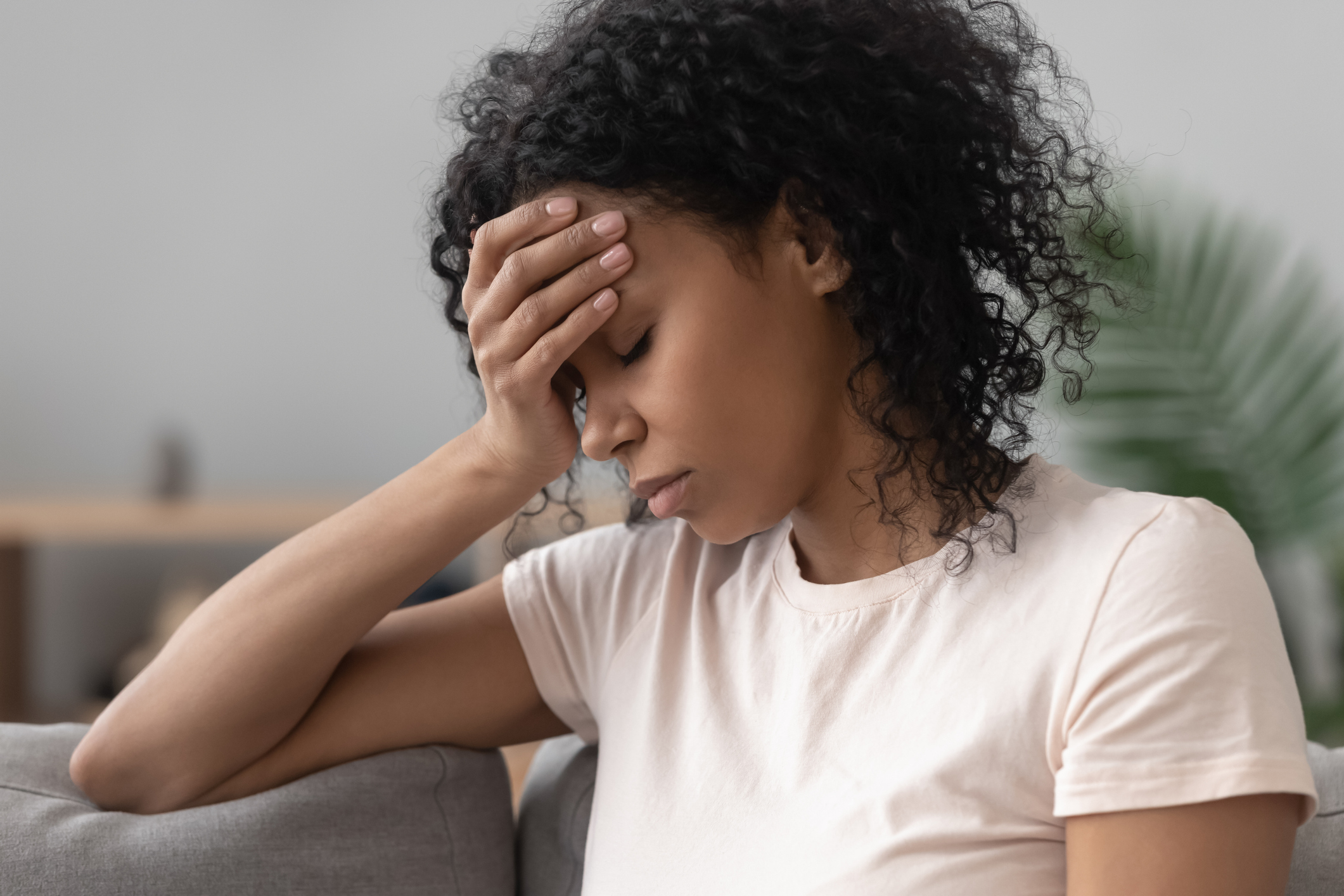 African woman sitting on couch feels unhappy having problems