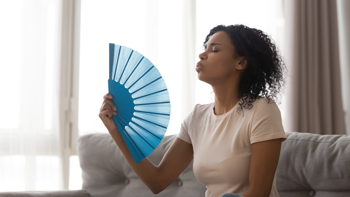 African woman cools herself with fan in hot weather