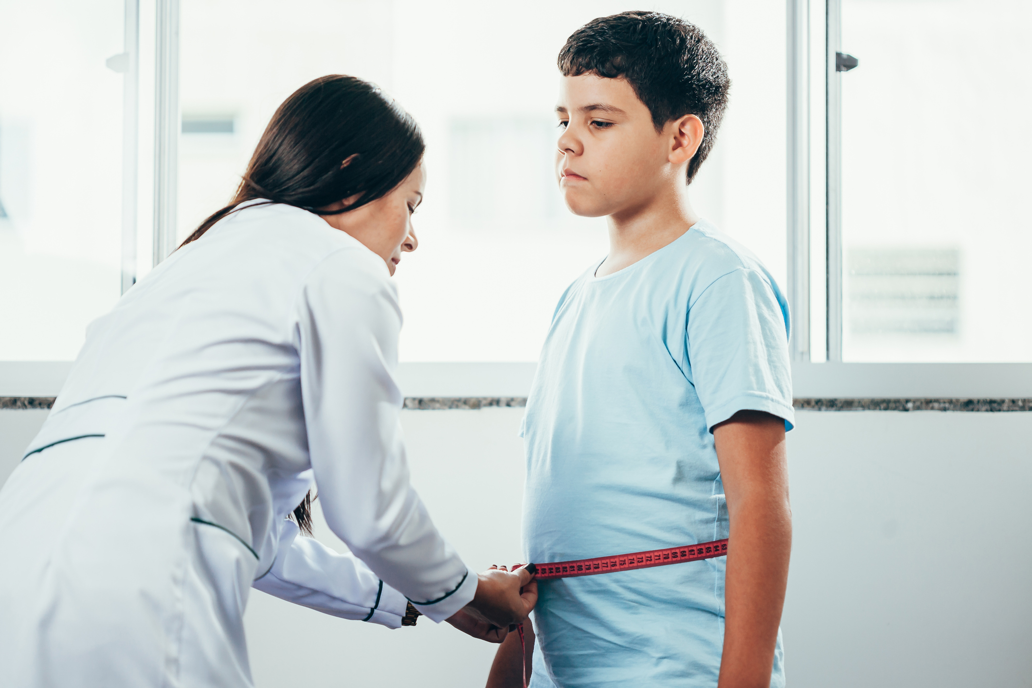 Female doctor measuring overweight boy in clinic