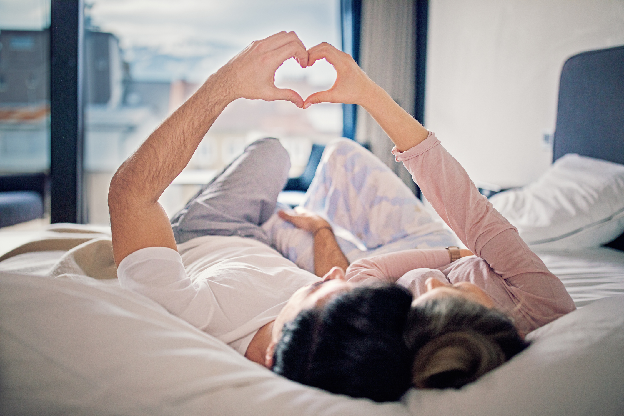 Couple is lying on the bed and making heart with their hands