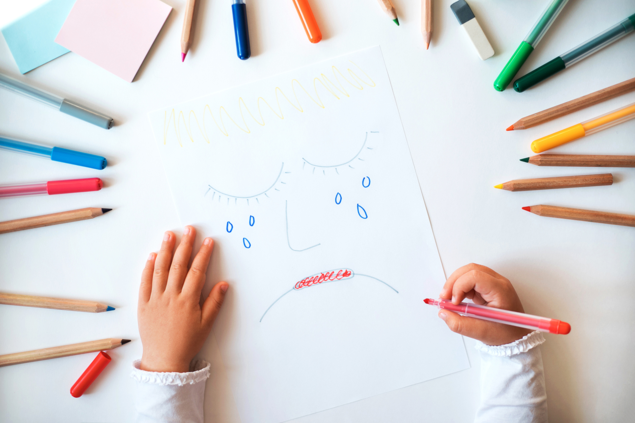 Child drawing sad face on the paper.