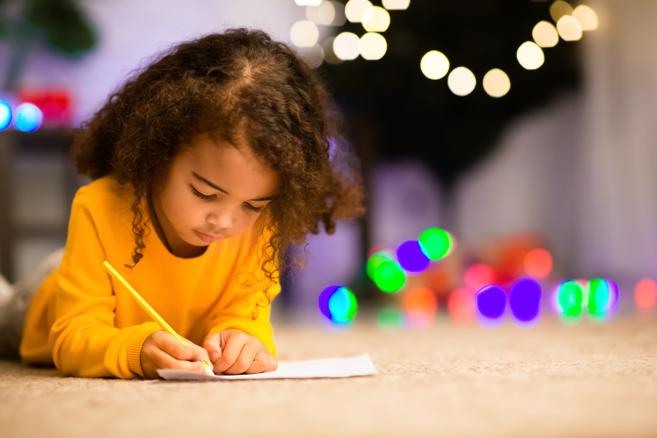 Little black girl drawing on floor near xmas tree