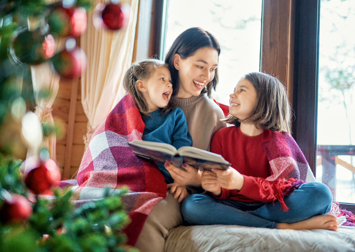 mother reading to daughters near Christmas tree.