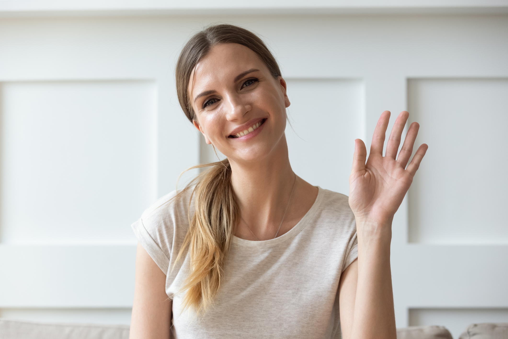 Happy pleasant young woman looking at camera, waving hello.