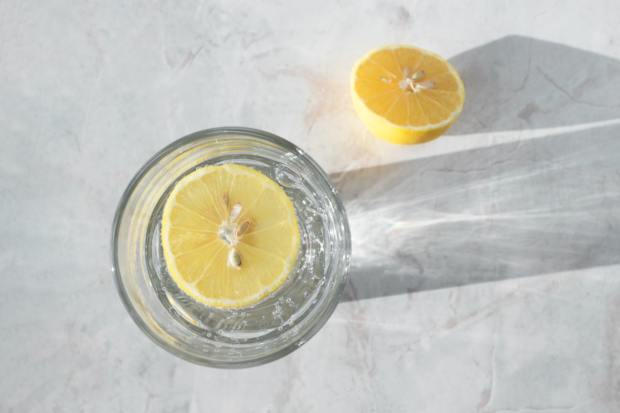 Soda water with slice of lemon in glass on marble table. Detox healthy drink concept, top view