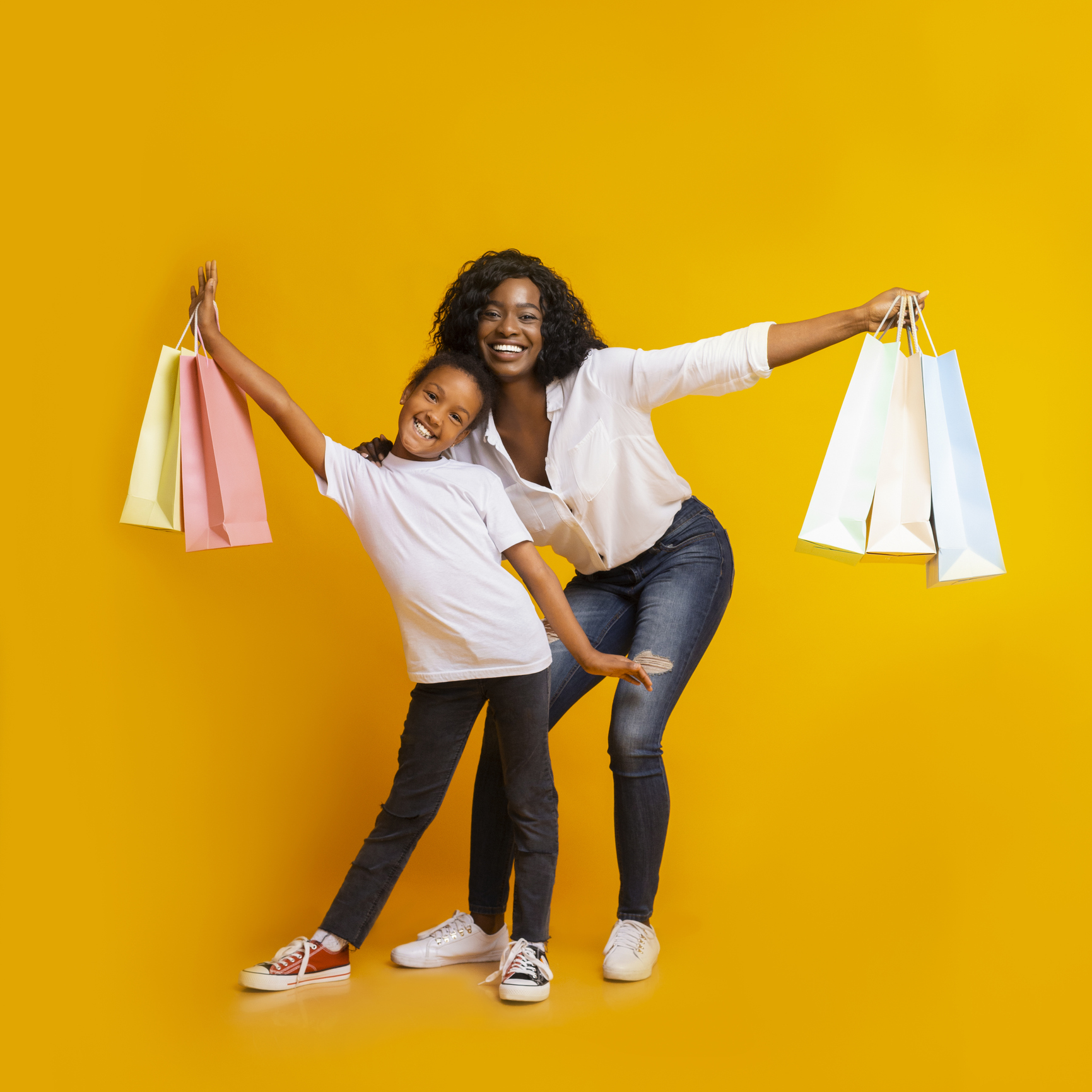 Portrait of cheerful black mom and daughter with colourful shopping bags