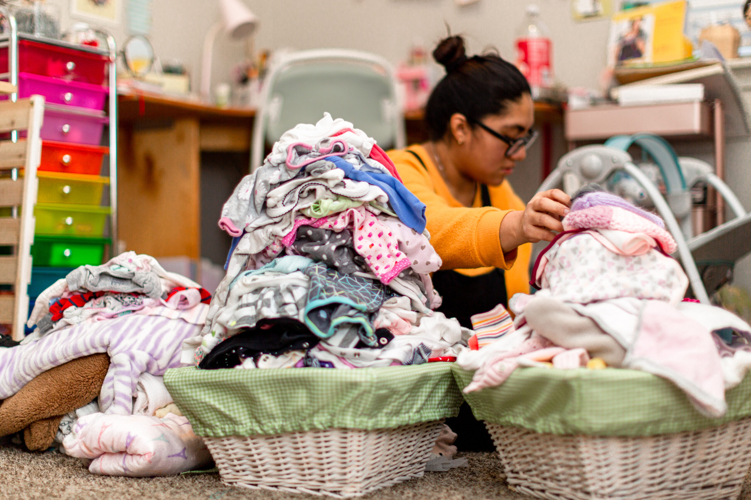 Hispanic Millennial Mother Overwhelmed With Piles of Baby Clothes