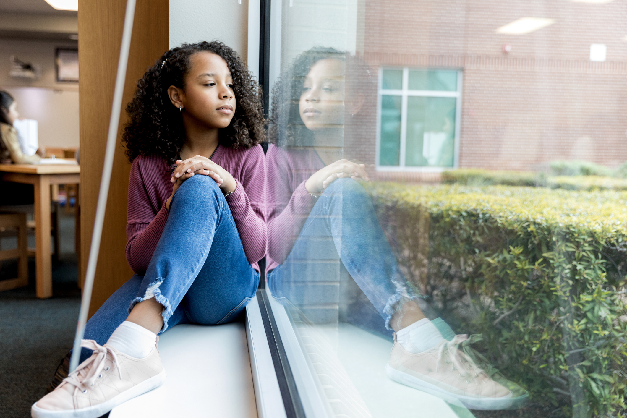 Young girl daydreams while looking out library window