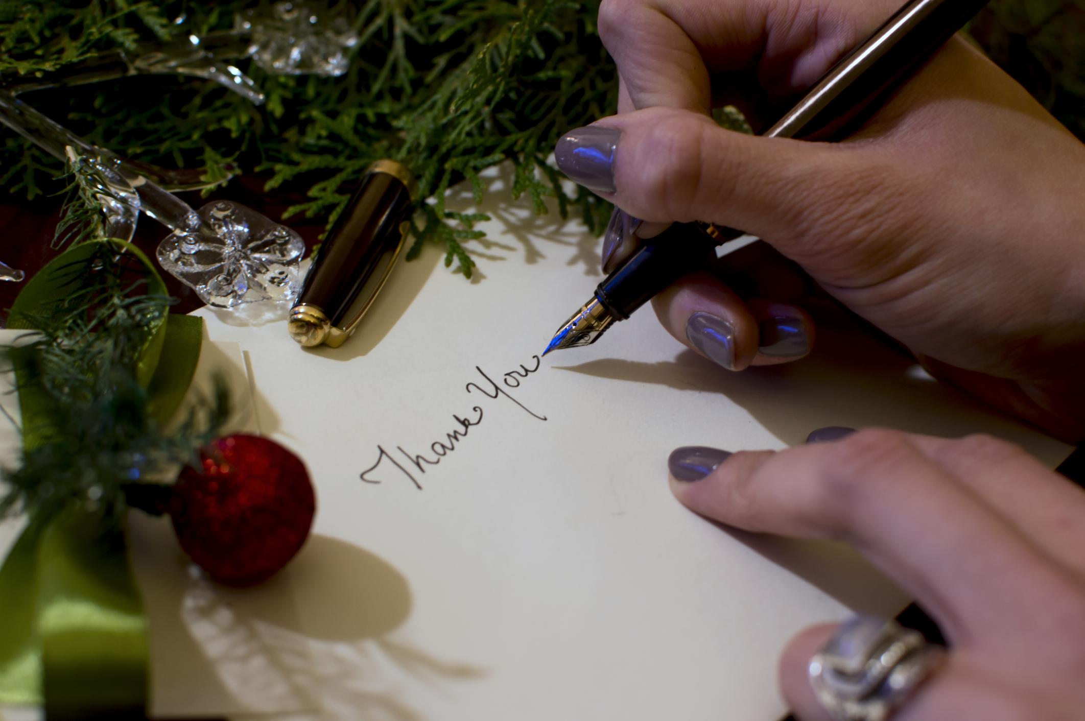 Woman writing Christmas card writing thank you with evergreen  and ornaments background