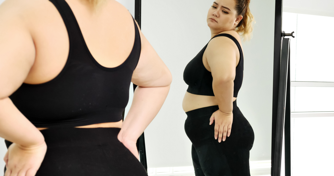 Chubby woman standing and looking at her stomach in a mirror.