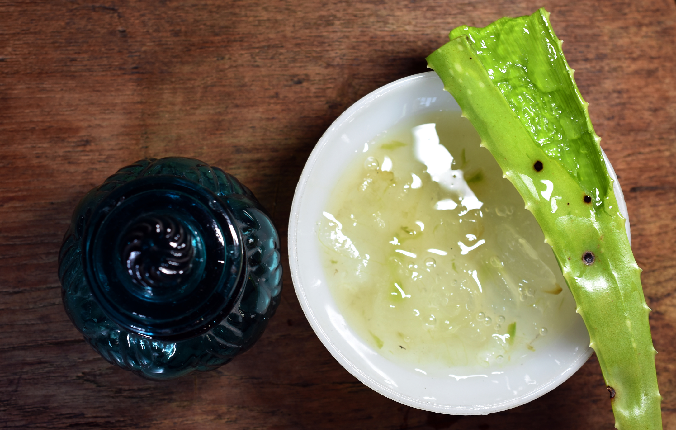 Fresh aloe vera gel in white bowl on the wooden table and antique blue glass small pot for keeping