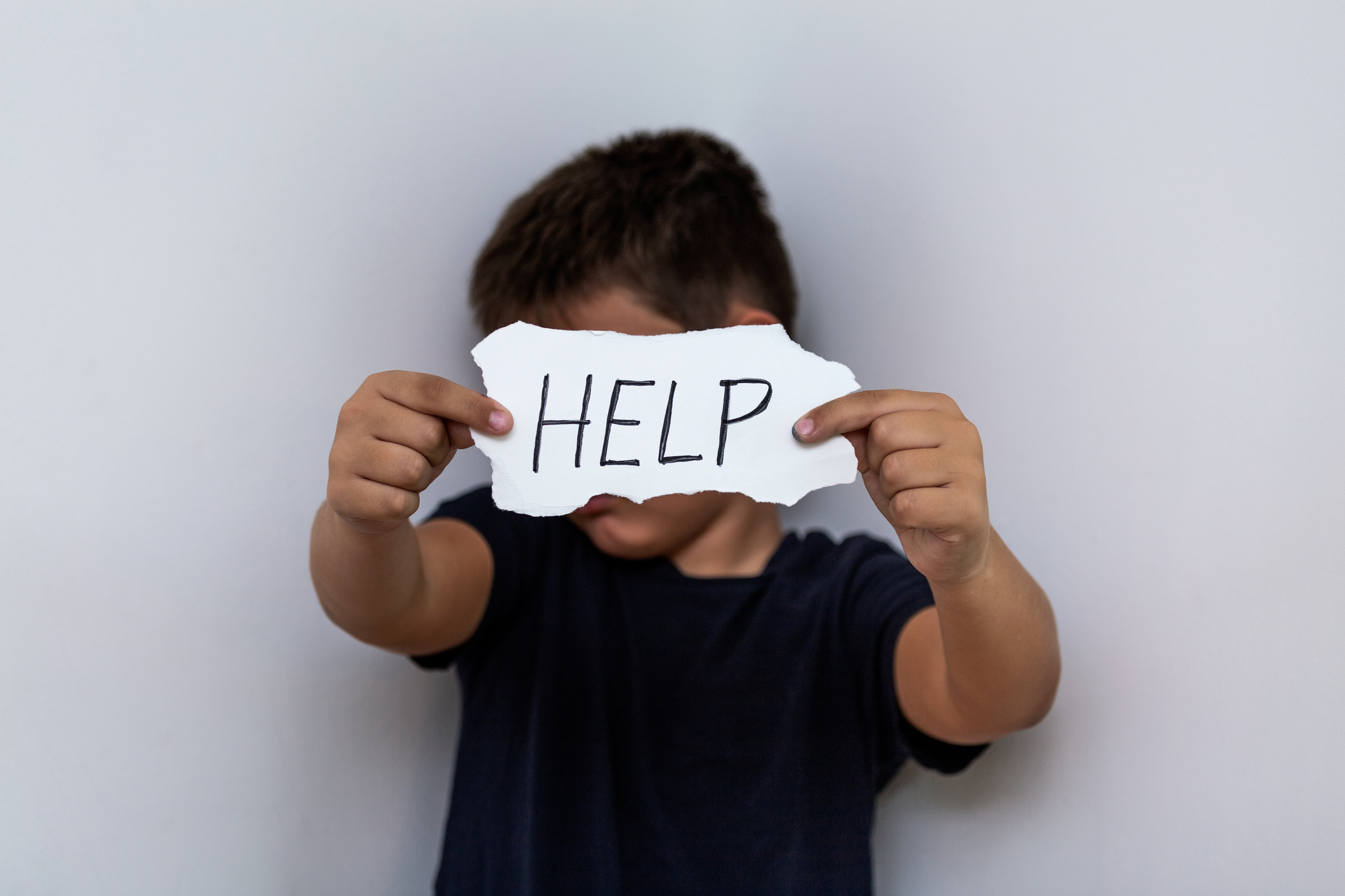 HELP, Teenager with help sign. Boy holding a paper with the inscription. Kid holding sheet of paper with word HELP on grey wall background.