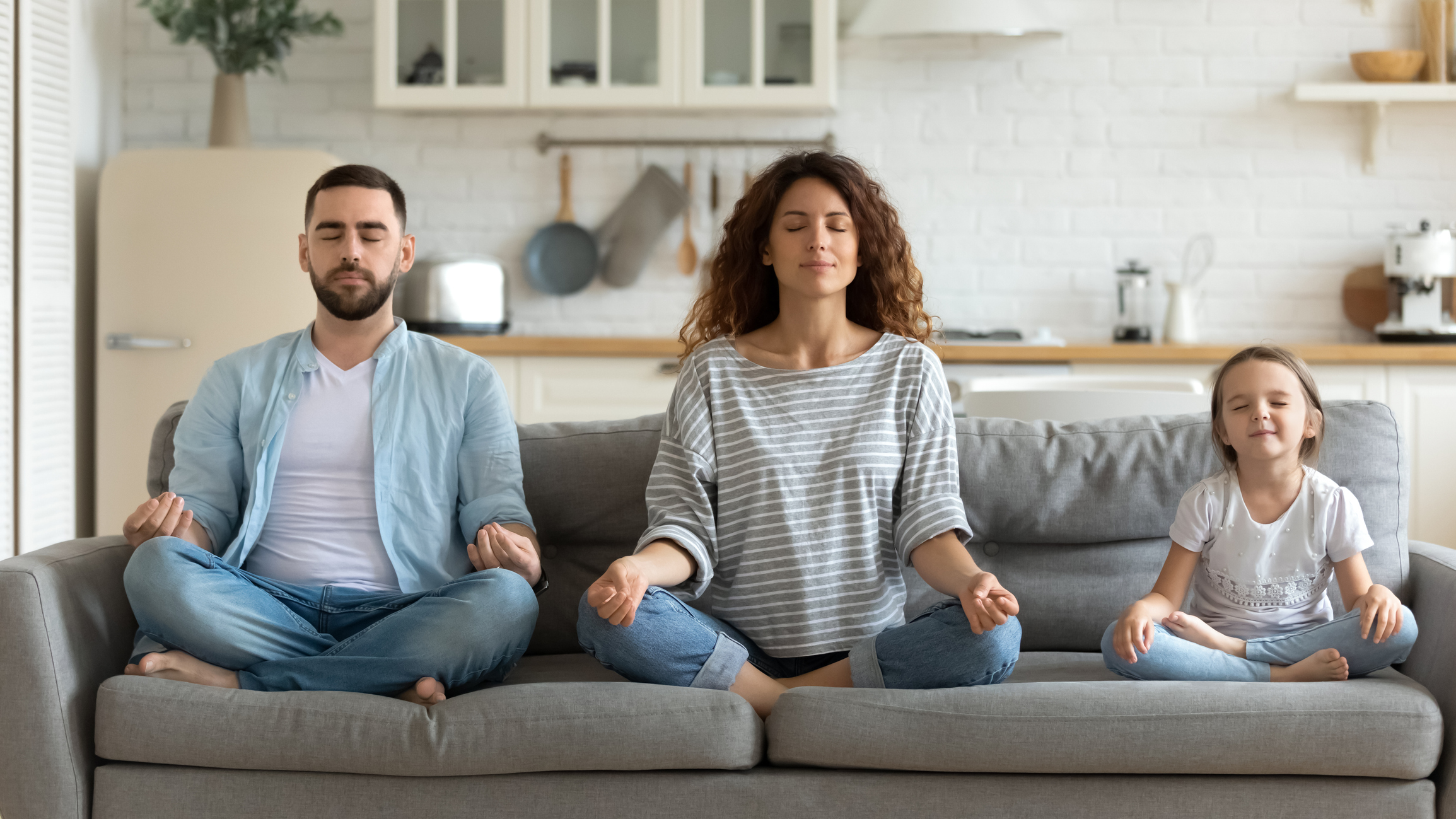 Couple and little daughter sitting on couch do meditation indoors