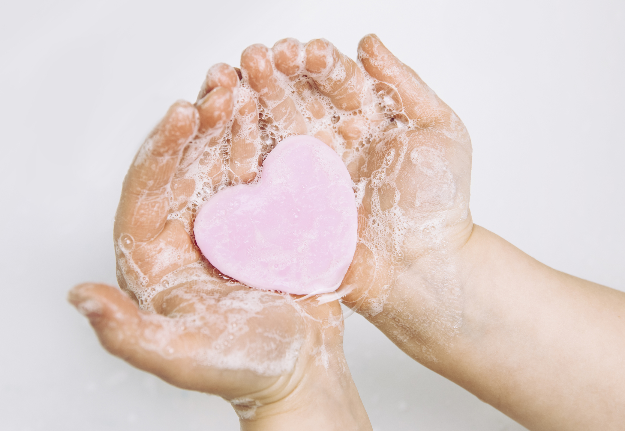 Importance of personal hygiene care. Flat lay view of child washing dirty hands with pink heart shape soap bar, lot of foam. Copy space.