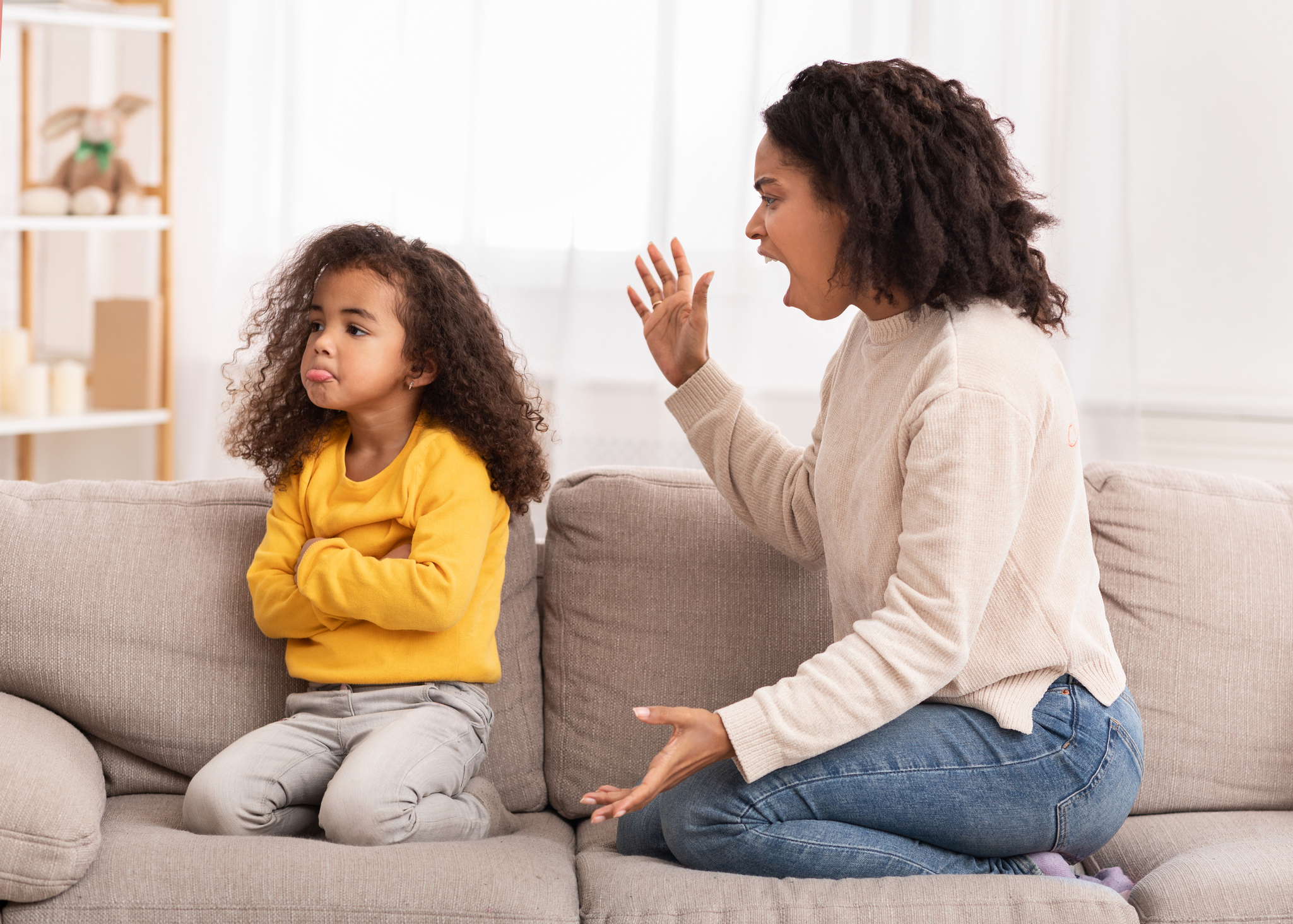 Angry Mother Shouting At Daughter Sitting On Couch At Home