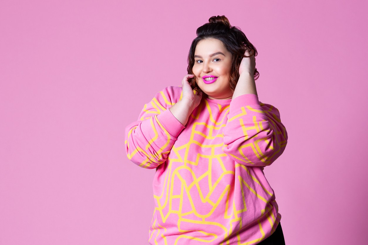 Happy plus size model in casual clothes, fat woman on pink background