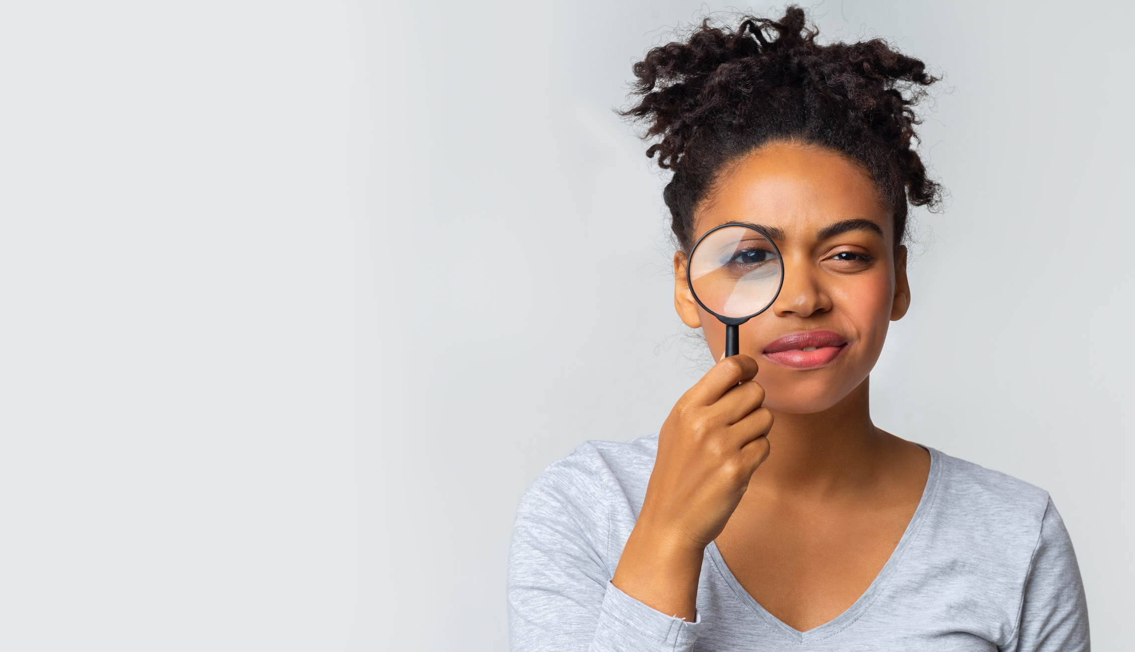 Curious girl holding magnifier over grey background