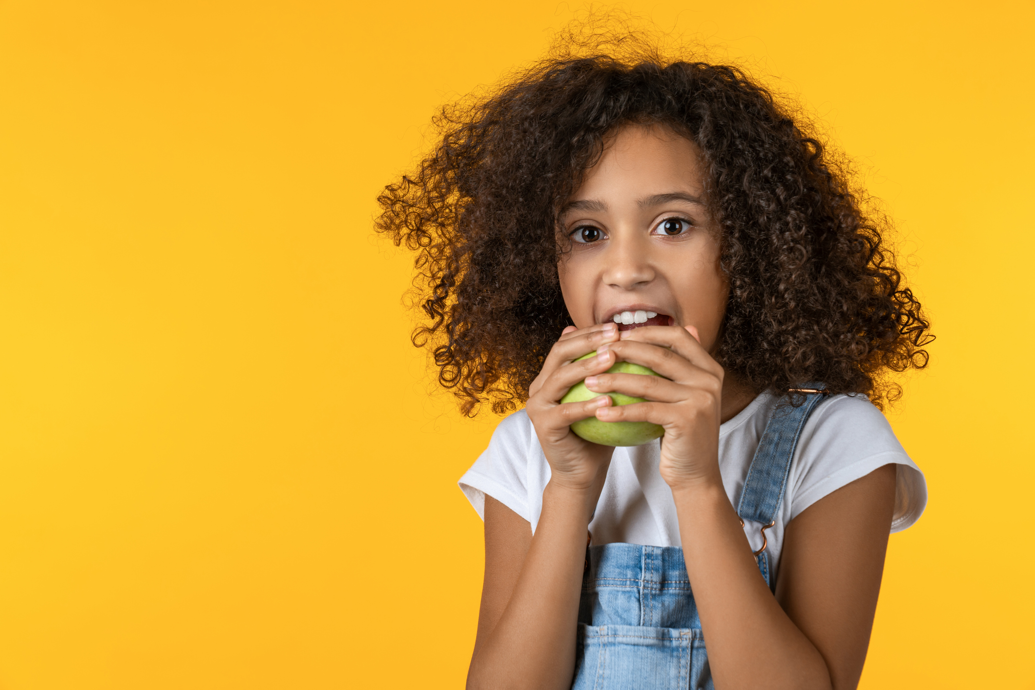 Little girl eating apple over yellow background