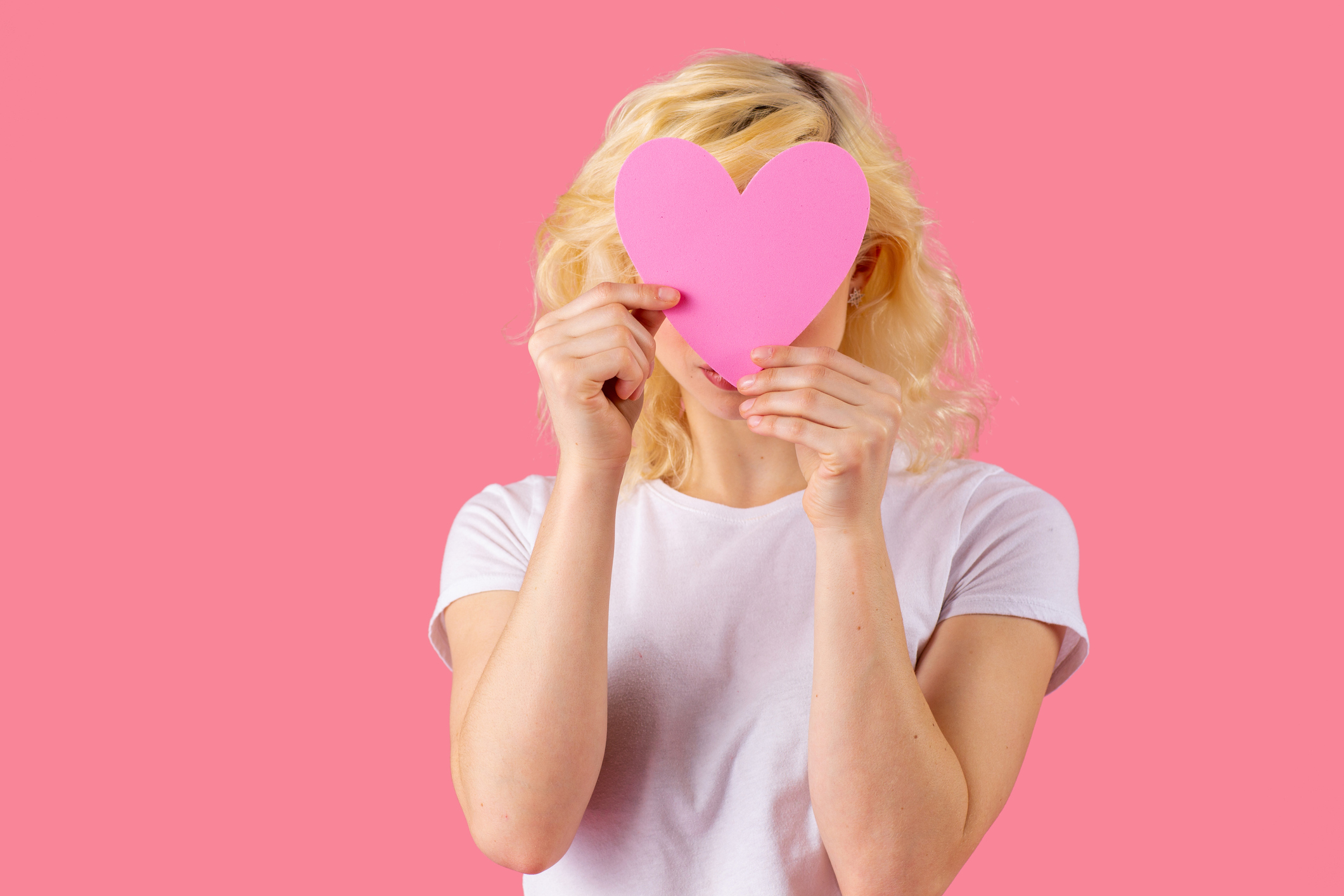 Studio portrait of a young woman holding pink heart covering head, love and dating concept