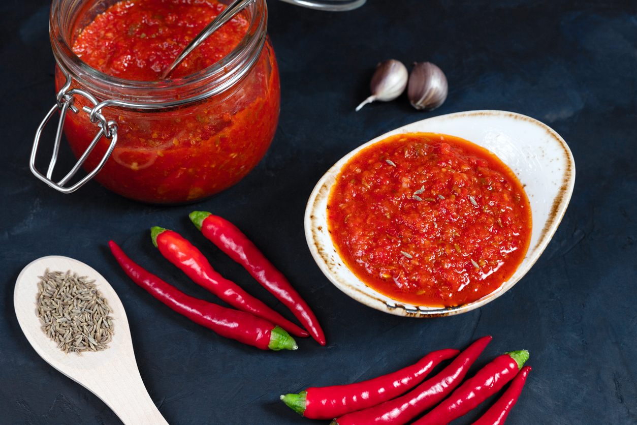 Hot chili pepper sauce paste harissa. Adjika on a blue background. Traditional Tunisia, Georgian and Arabic cuisine.