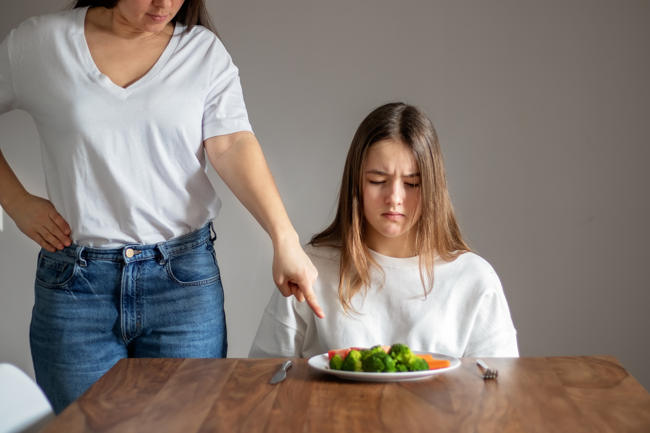 No vegan diet concept. Mother forces her teen daughter to eat healthy food -  broccoli and other vegetables. Food waste.