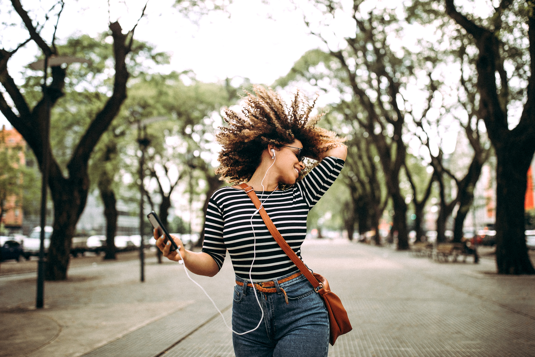 Happy Hispanic woman listening to music and dancing on the street