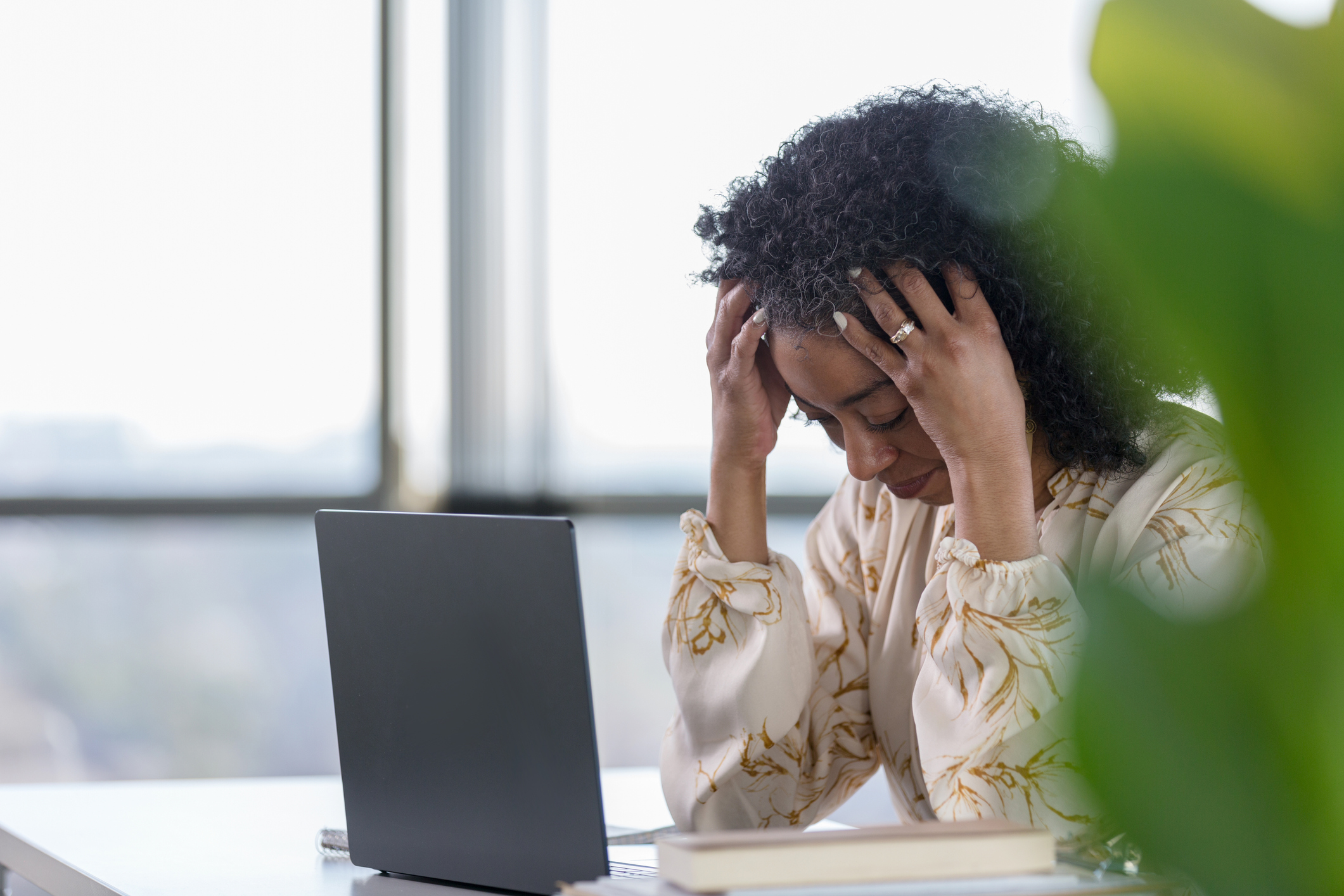 Mature woman holds head in hands while sitting at desk