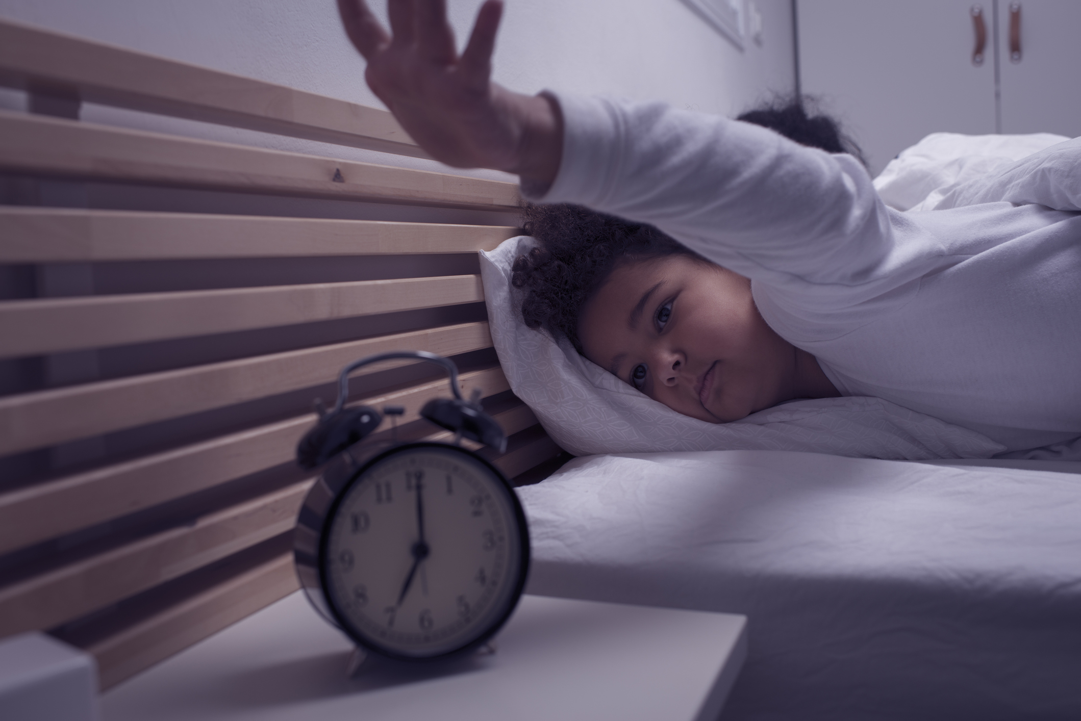 Sleepy little girl switching off her alarm clock.