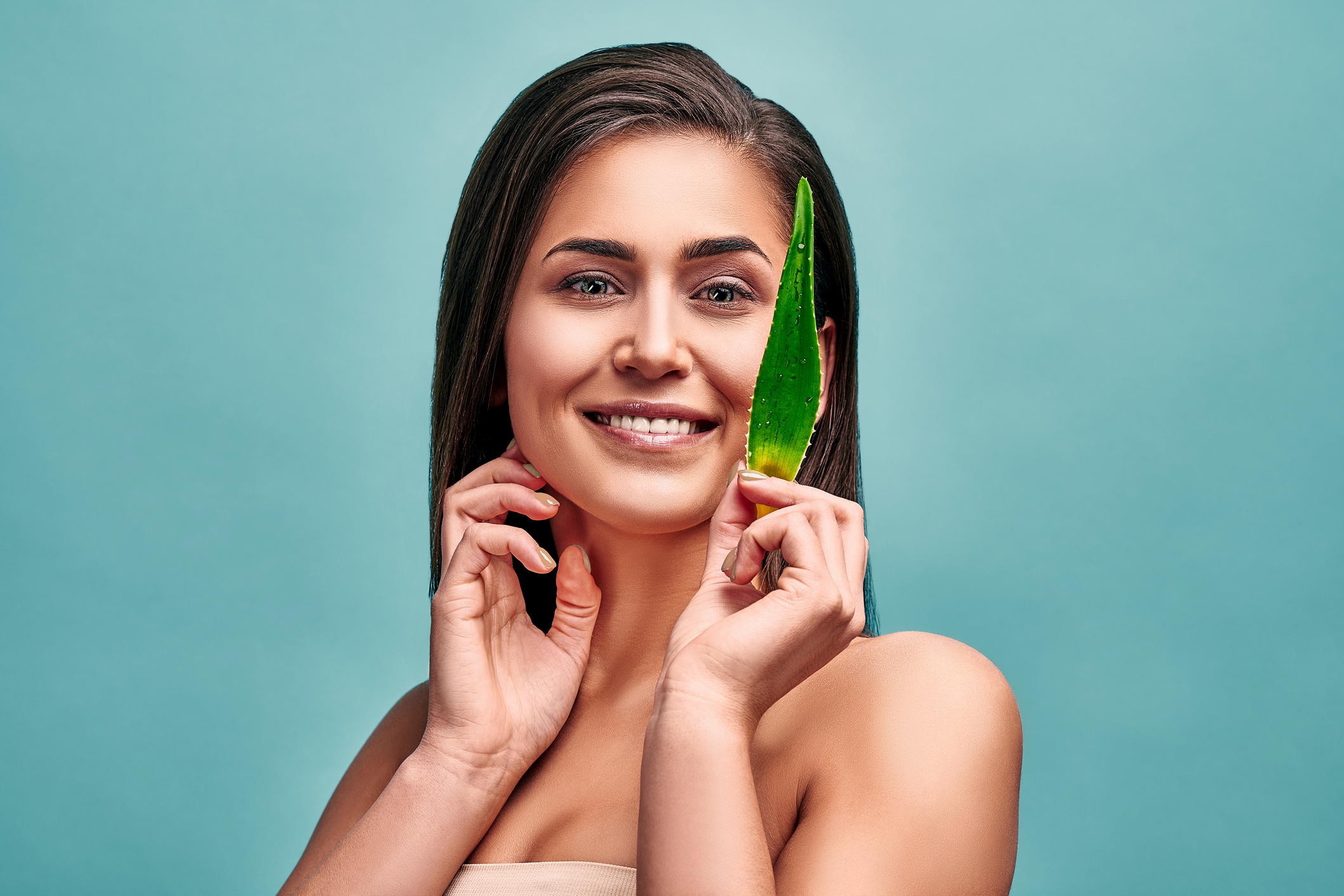 I choose the right care for my skin! Beautiful woman posing with a leaf of aloe in the studio on an aquamarine background.