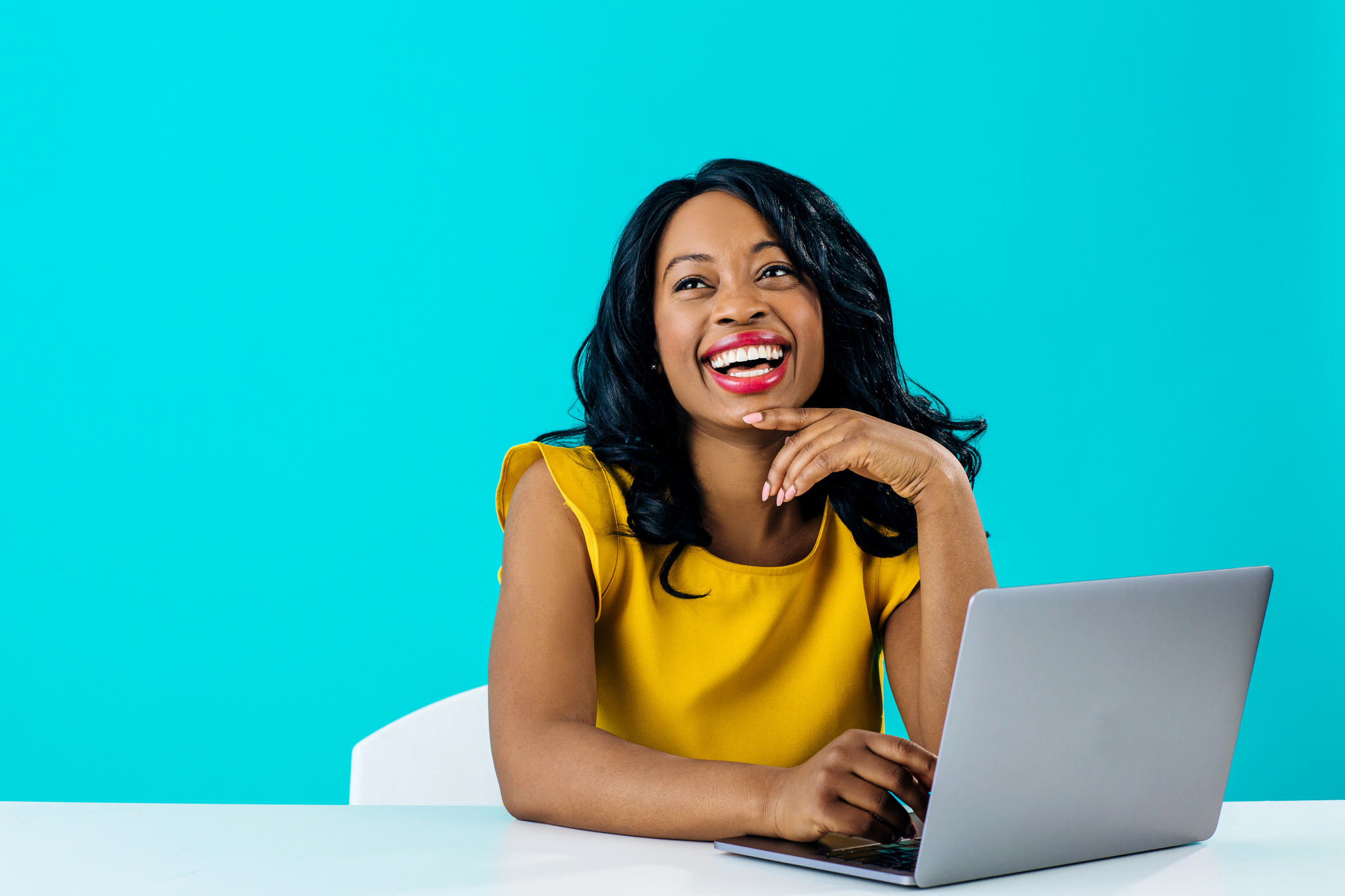 Portrait of a happy young smiling woman sitting behind desk and computer laptop, looking up