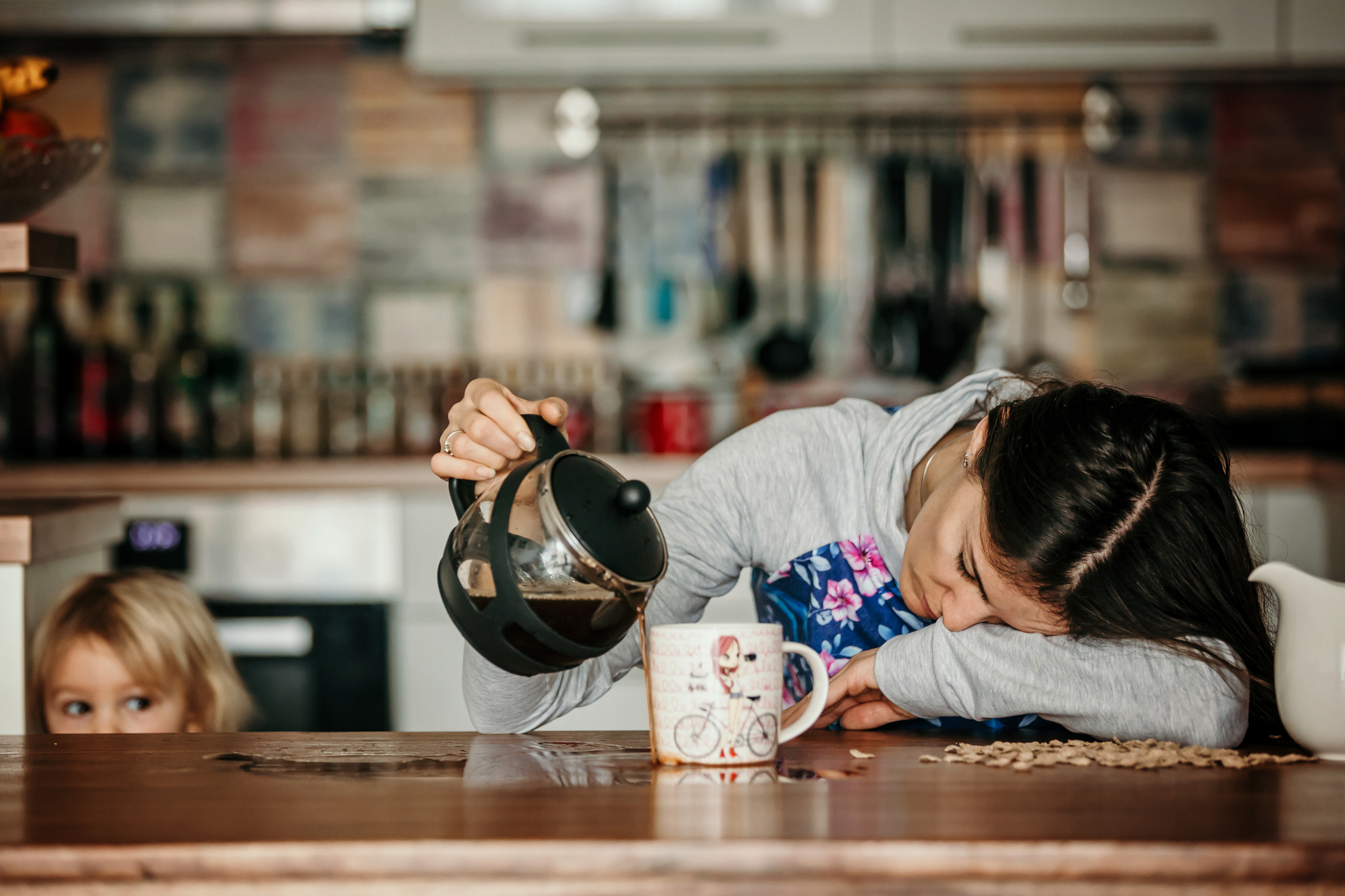 Tired mother, trying to pour coffee in the morning. Woman lying on kitchen table after sleepless night