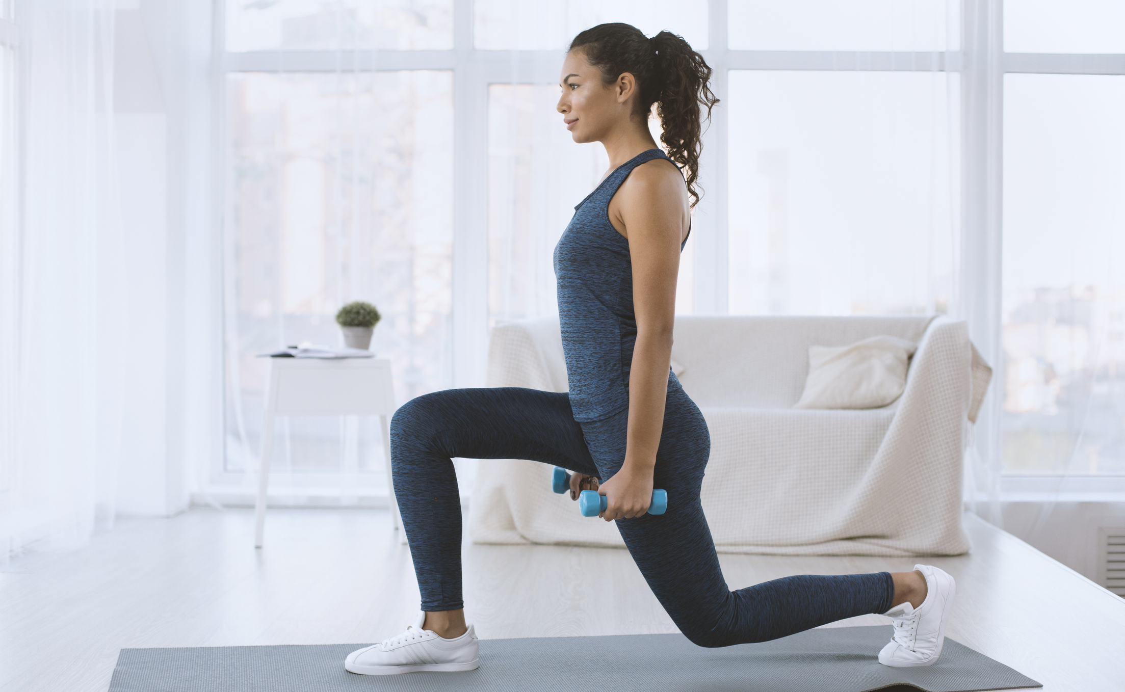 Slim Hispanic girl doing lunges with dumbbells at home, empty space